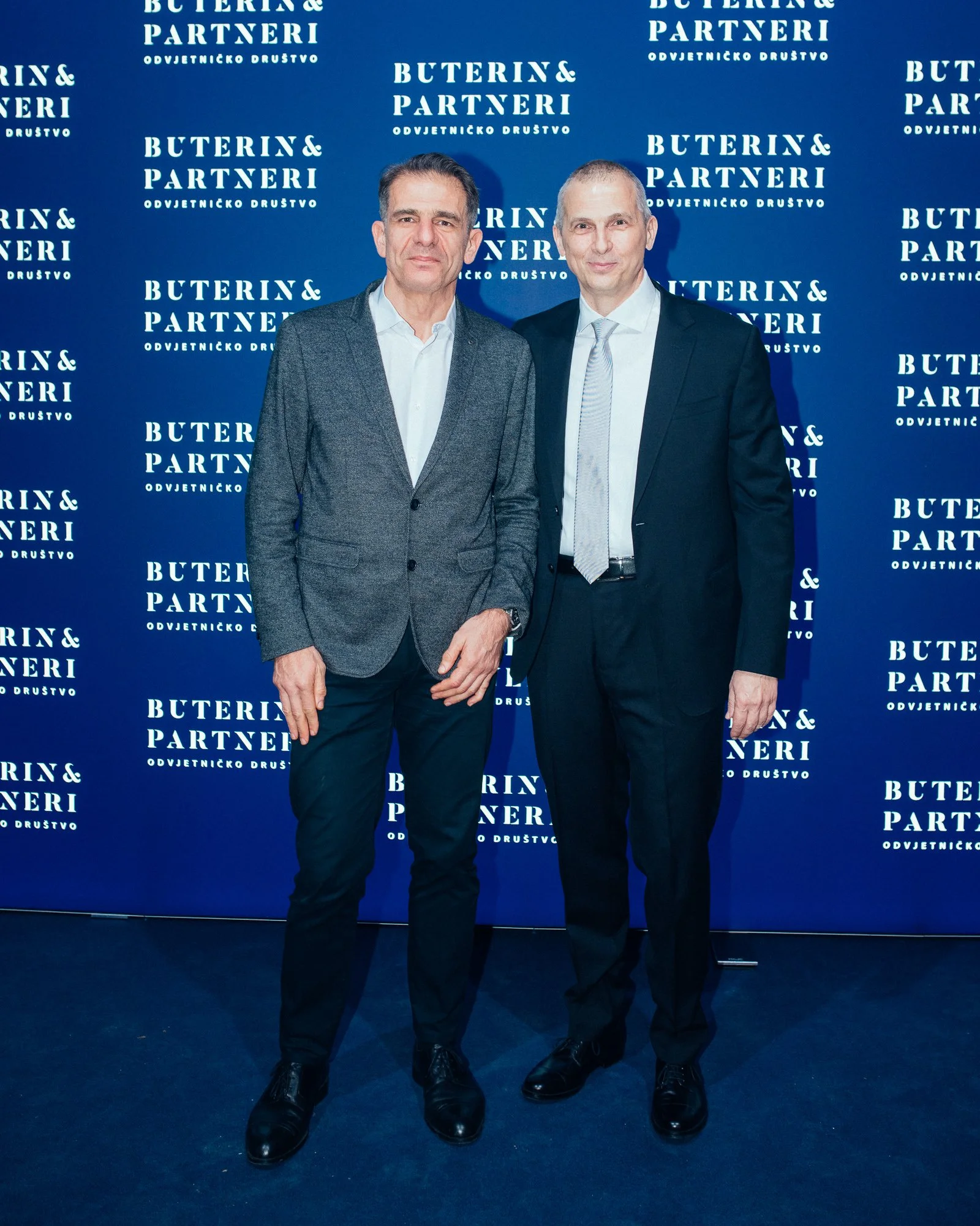 Two men in business suits standing in front of a blue backdrop with white text that reads "Buterin & Partneri, Odvjetničko društvo."