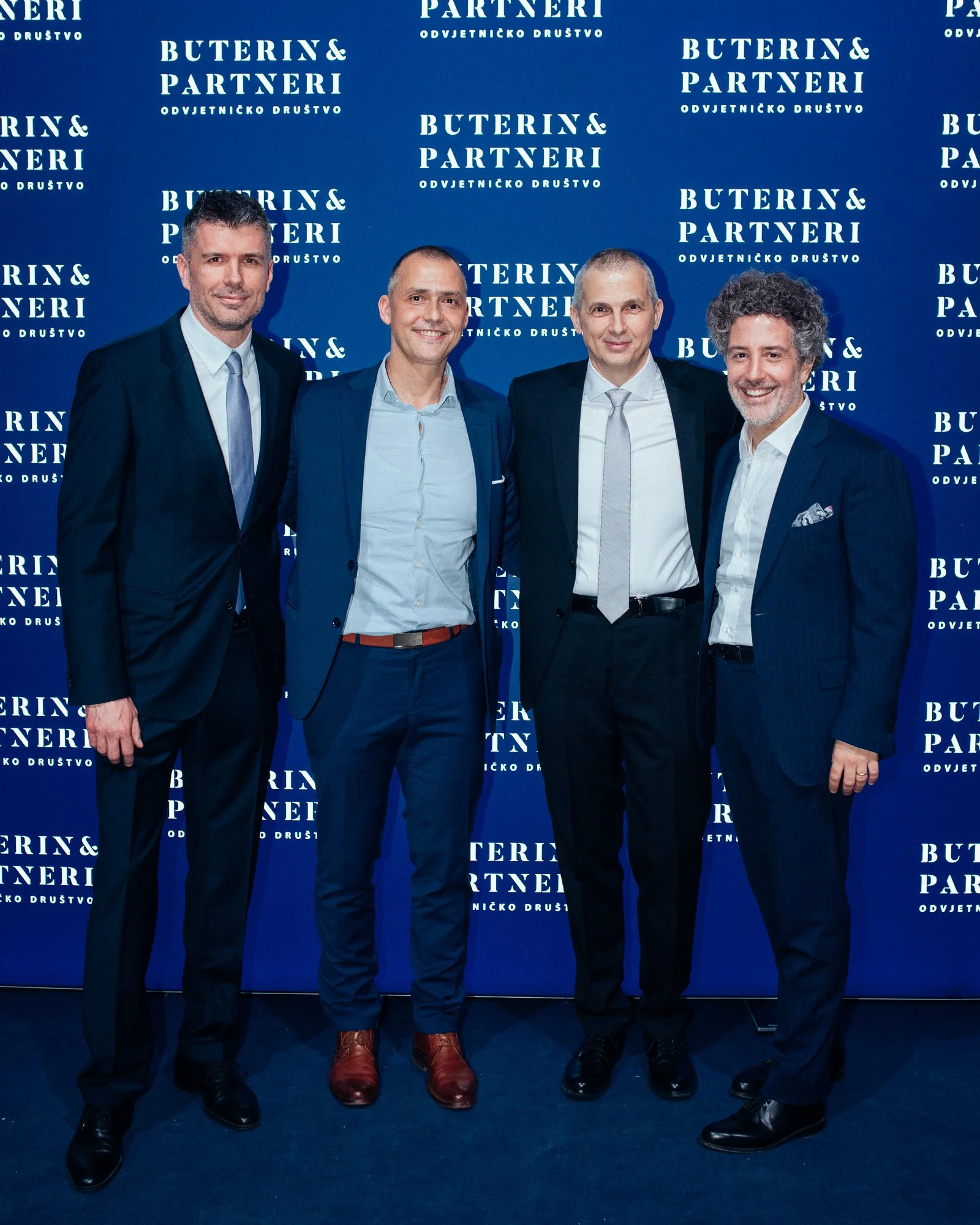 Four men in suits standing together in front of a blue backdrop with the text 'Buterin & Partneri'.