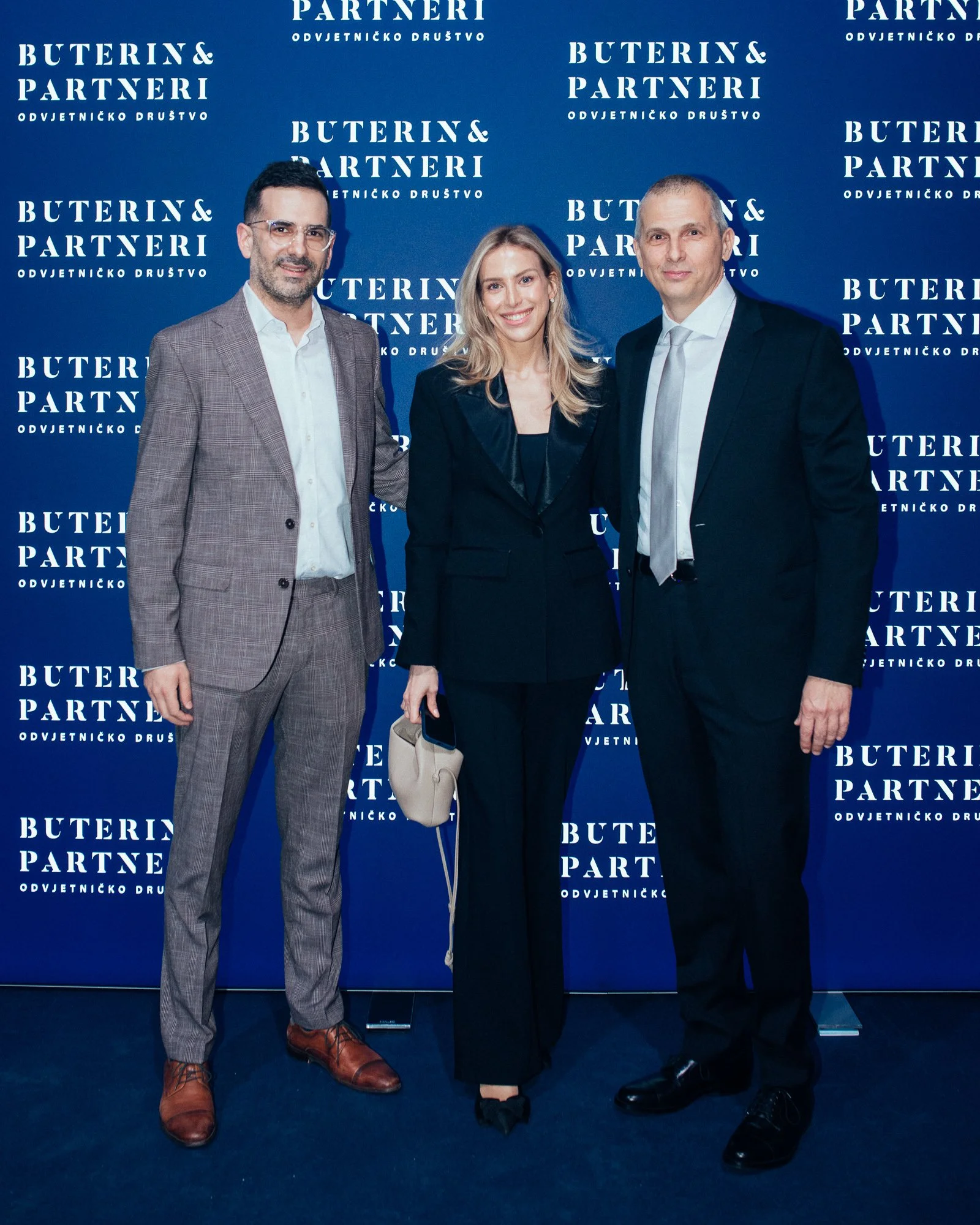 Three people dressed formally standing in front of a blue backdrop with 'Buterin & Partneri' branding, smiling for a photo.