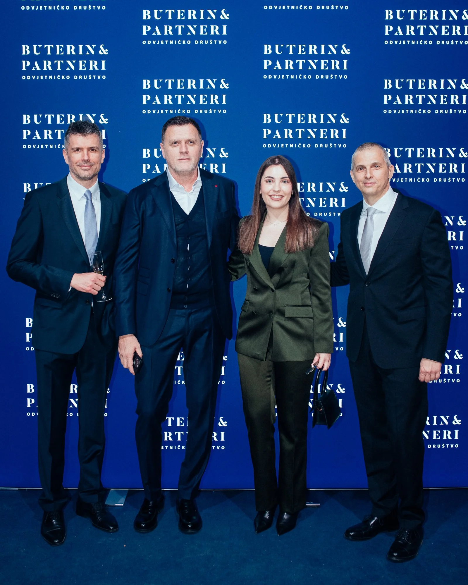 Four professionally dressed individuals standing in front of a blue backdrop with white text that reads 'BUTERIN & PARTNERI' and 'ODVJETNIČKO DRUŠTVO'. They are posing for a photo at what appears to be a formal event or conference, with three men and