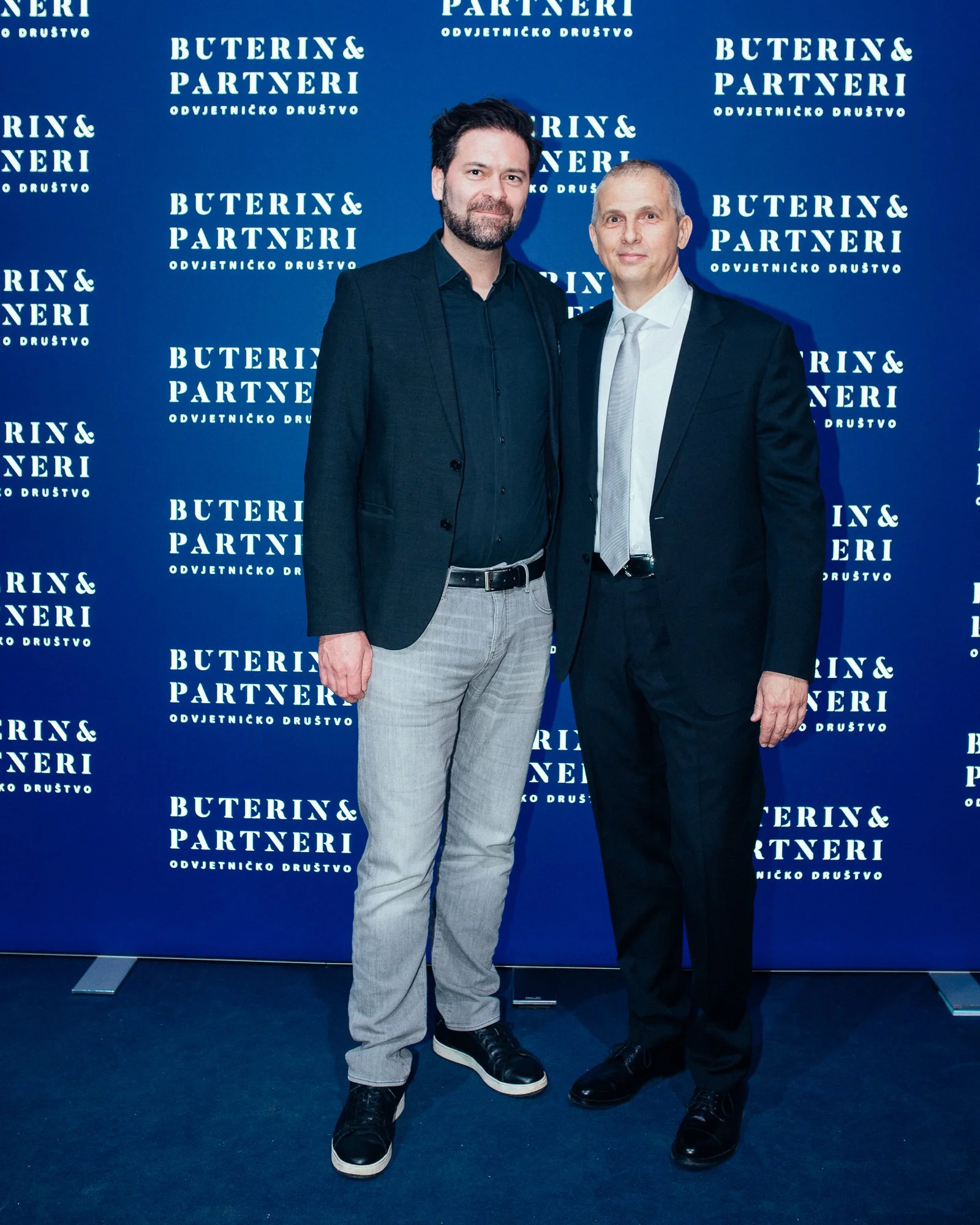 Two men in formal suits standing in front of a blue backdrop with white text that reads 'Buterin & Partneri Odvjetničko Društvo.'