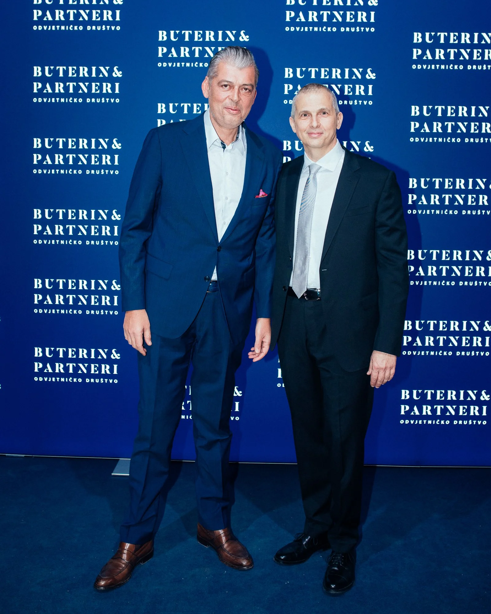 Two men in suits standing together in front of a blue backdrop with white text that reads 'BUTERIN & PARTNERI ODVJETNICKO DRUŠTVO'.
