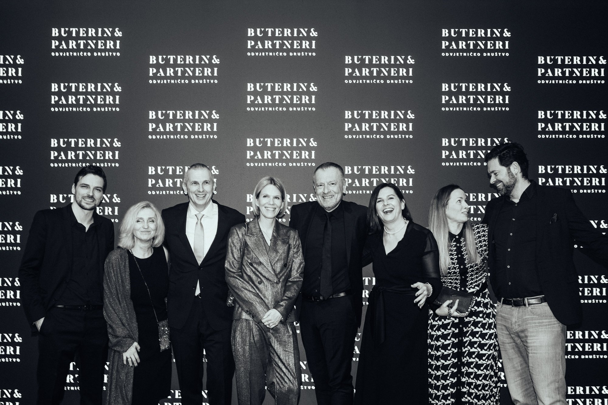 A group of nine people, six women and three men, standing together in front of a backdrop with the text 'BUTERIN & PARTNERI ODVJETNIČKO DRUŠTVO' repeated multiple times, smiling and posing for a photo.
