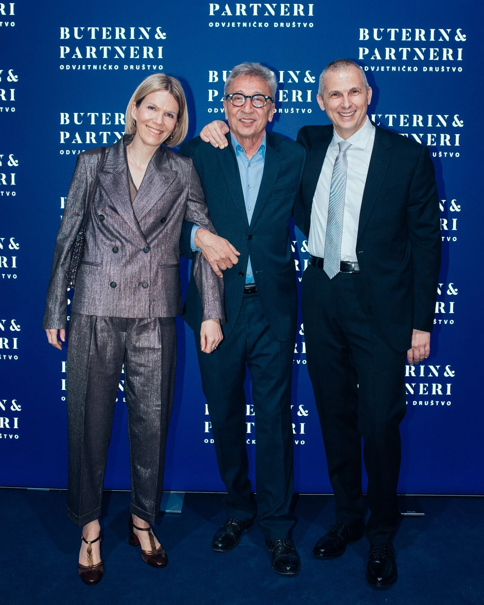 Three professionally dressed individuals, two men and a woman, standing together in front of a blue backdrop with white text that reads "BUTERIN & PARTNERI" and "ODVJETNIČKO DRUŠTVO." They are smiling and posing for a photo.