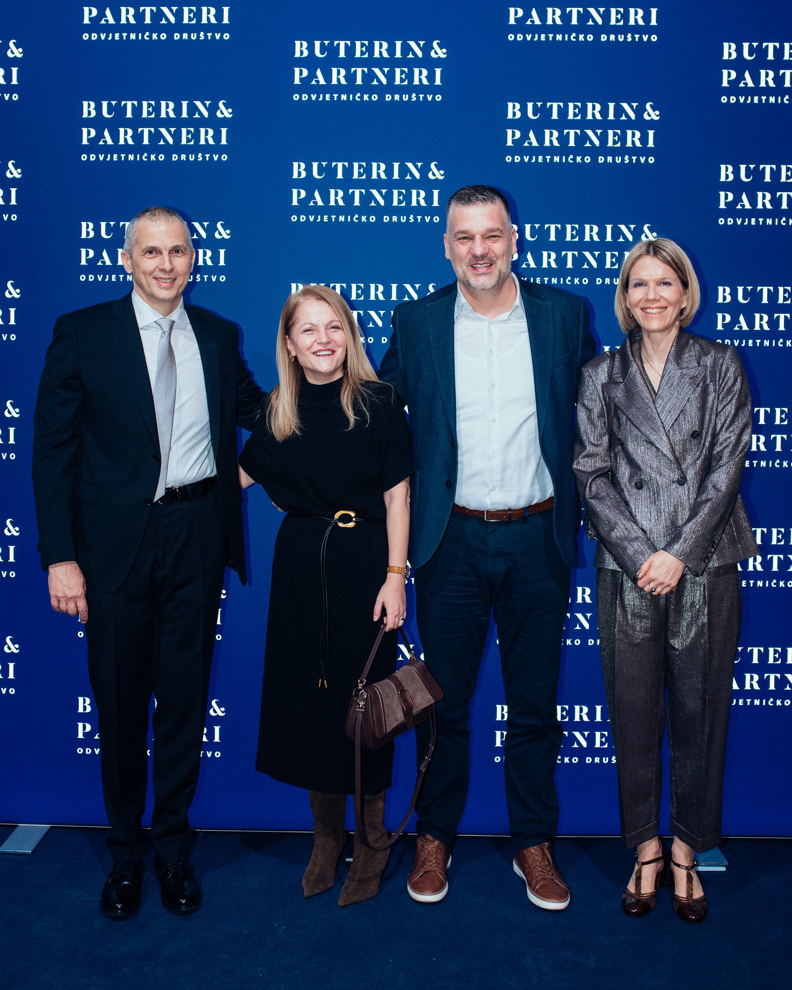 Four people in formal attire standing in front of a blue backdrop with white text that reads 'BUTERIN & PARTNERI ODVJETNIČKO DRUŠTVO', with two men and two women smiling at the camera.