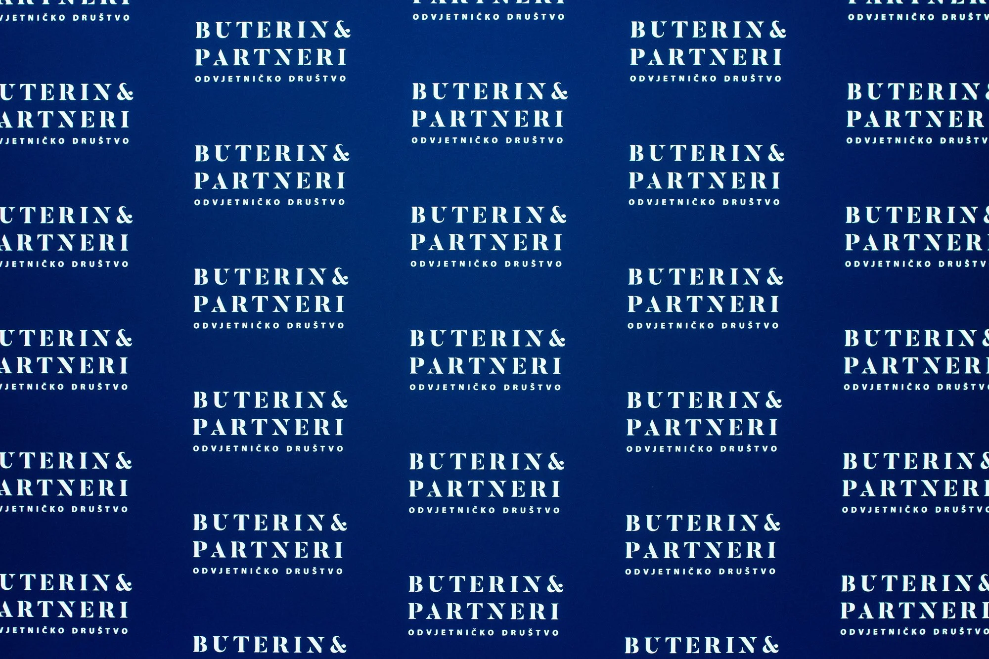 Patterned blue backdrop with repeating white text that says 'Buterin & Partneri' and a smaller line in Croatian or similar language below, reading 'Odvjetničko društvo'.