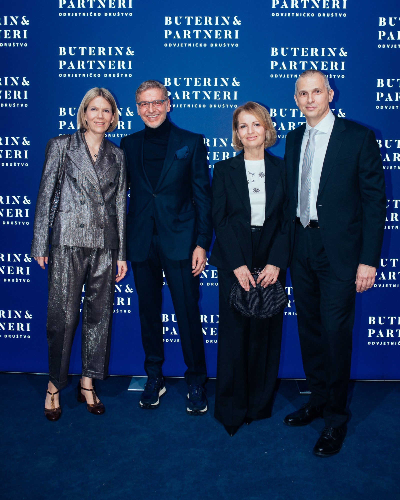Four professionally dressed individuals standing in front of a blue background with repeating white text that reads 'Buterin & Partneri Odvjetničko Društvo.'
