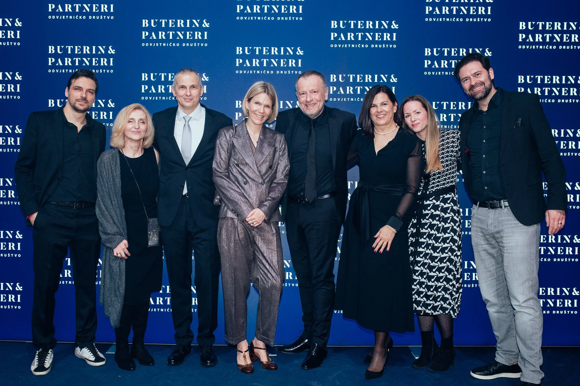Group of eight people standing in front of a blue backdrop with the words 'Buterin & Partneri' repeated, posing for a photo at a formal event.