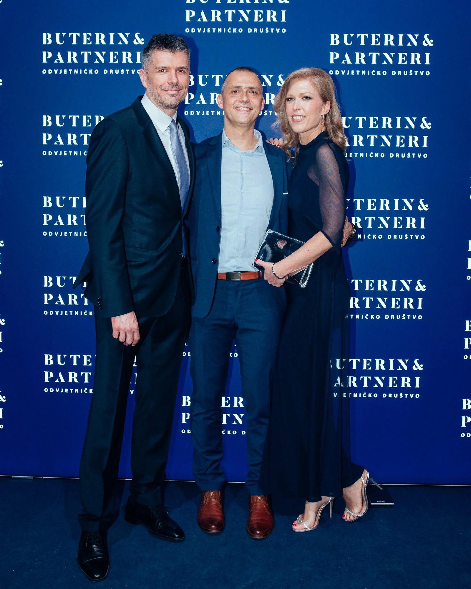 Three people dressed in formal attire standing in front of a blue backdrop with white text that reads 'BUTERIN & PARTNERI ODVJETNIČKO DRUŠTVO'.