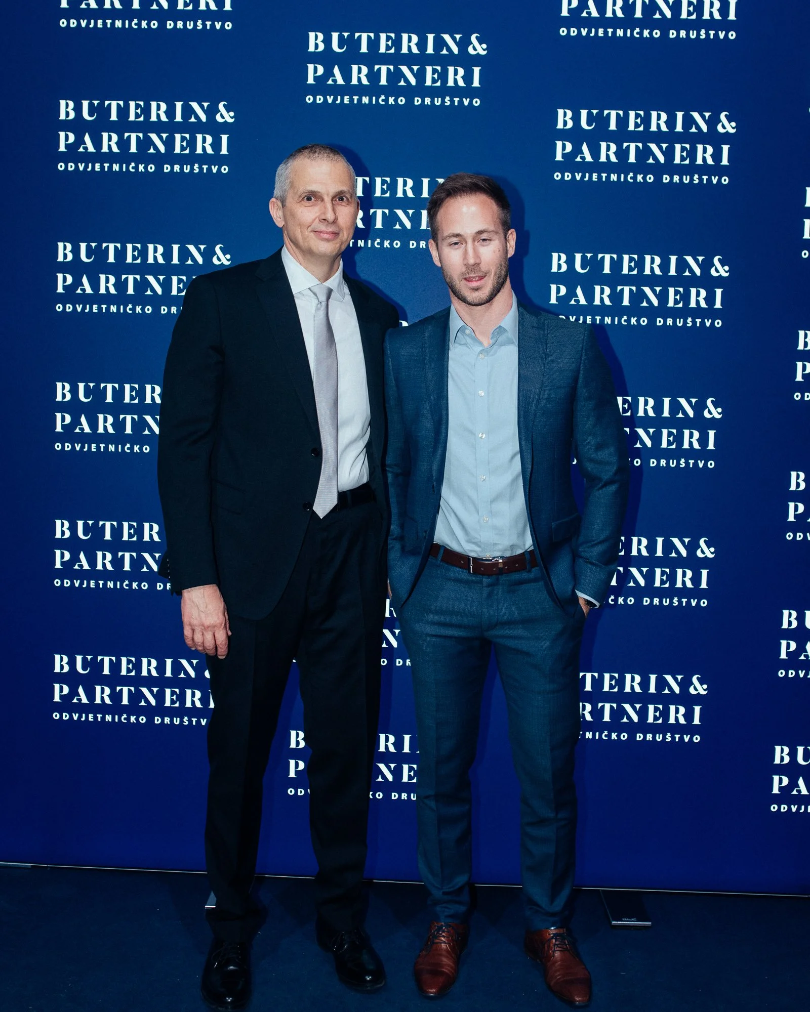 Two men in business suits standing in front of a blue backdrop with white text that reads "Buterin & Partneri Odvjetničko Društvo."