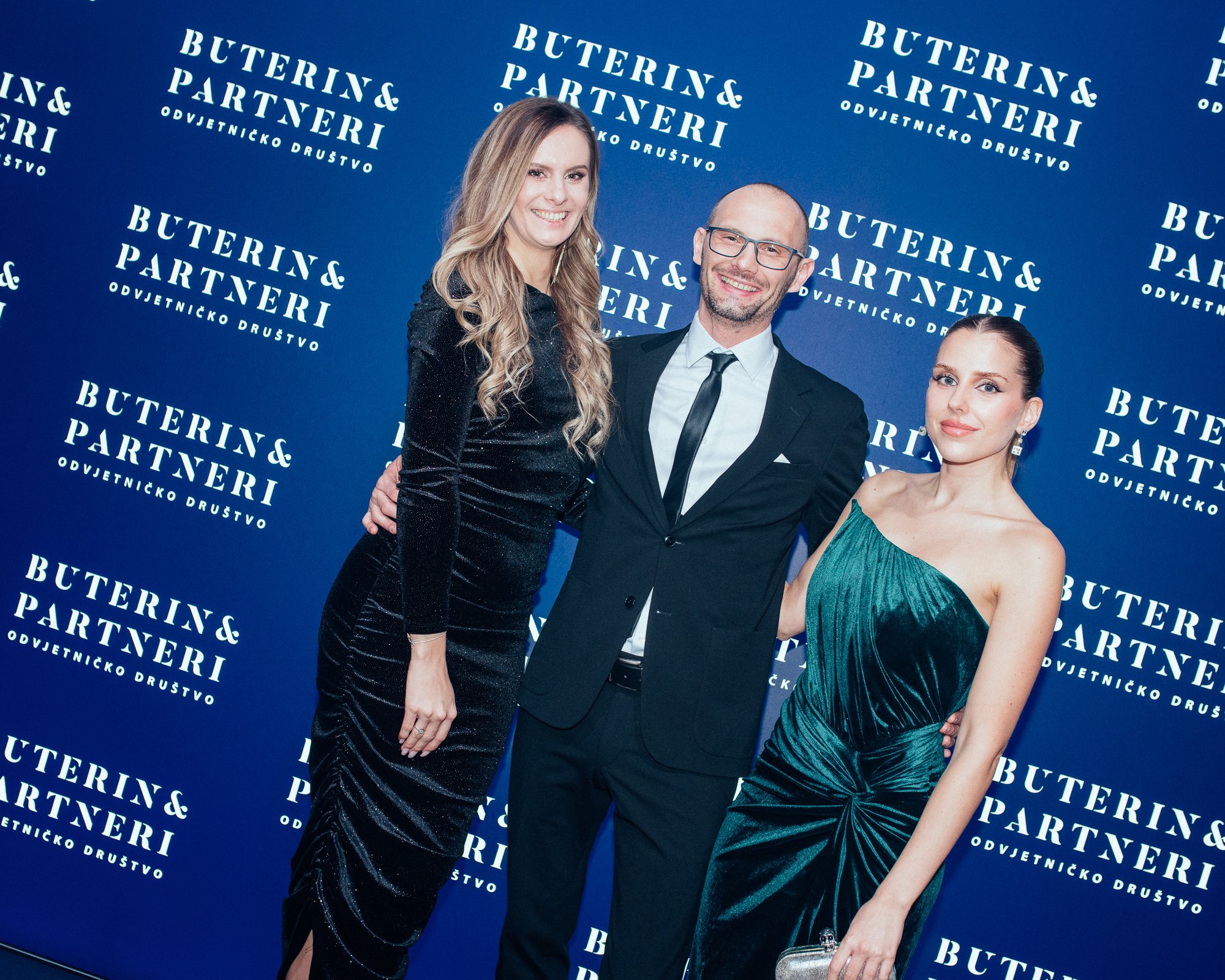 Three people dressed formally, two women and one man, smiling and posing in front of a blue backdrop with white text that reads 'BUTERIN & PARTNERI ODVJETNICKO DRUŠTVO'.
