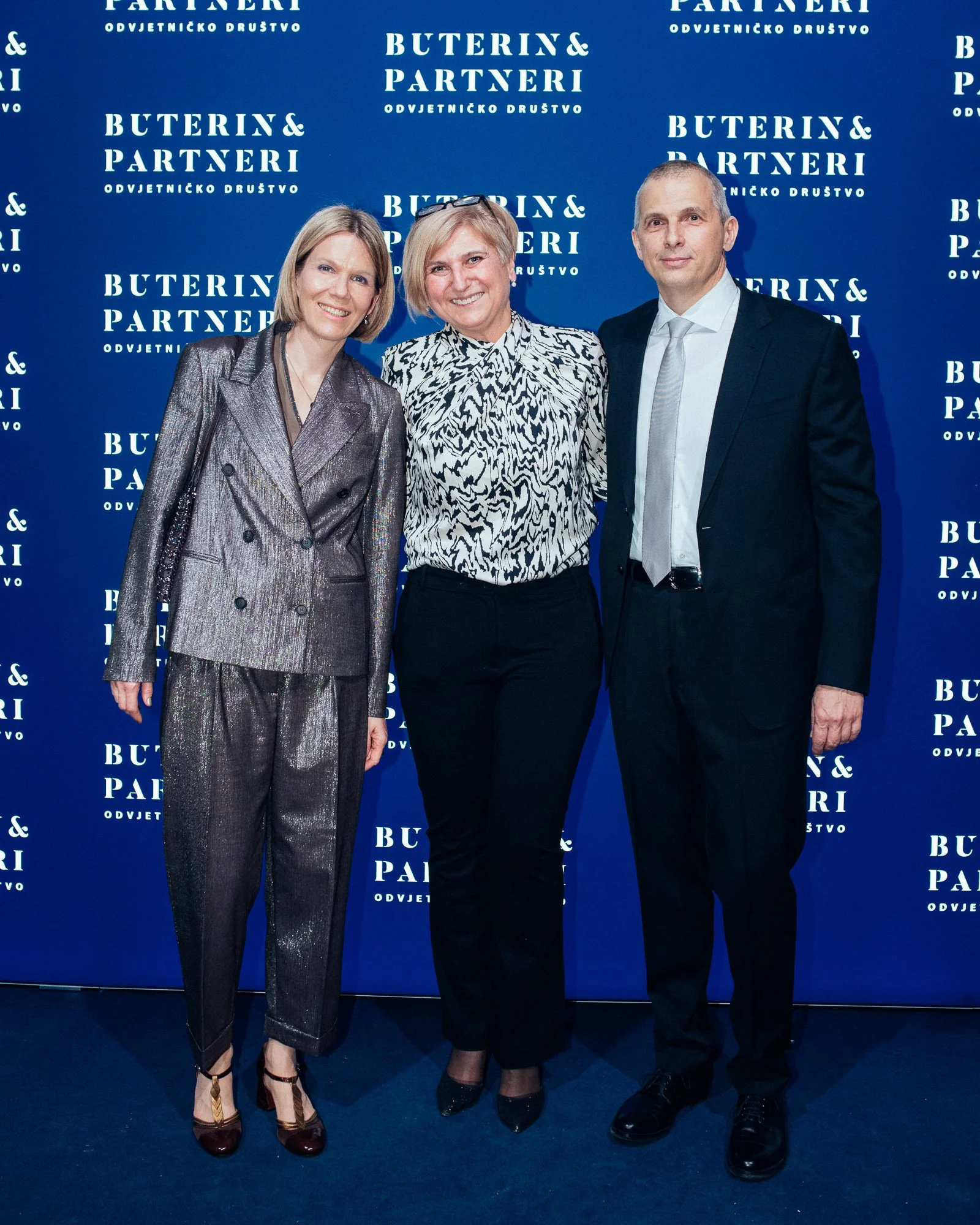 Three people standing in front of a blue backdrop with white text that reads 'Buterin & Partneri Odvjetničko Društvo'. The group consists of two women and one man, dressed in formal attire, smiling at the camera.