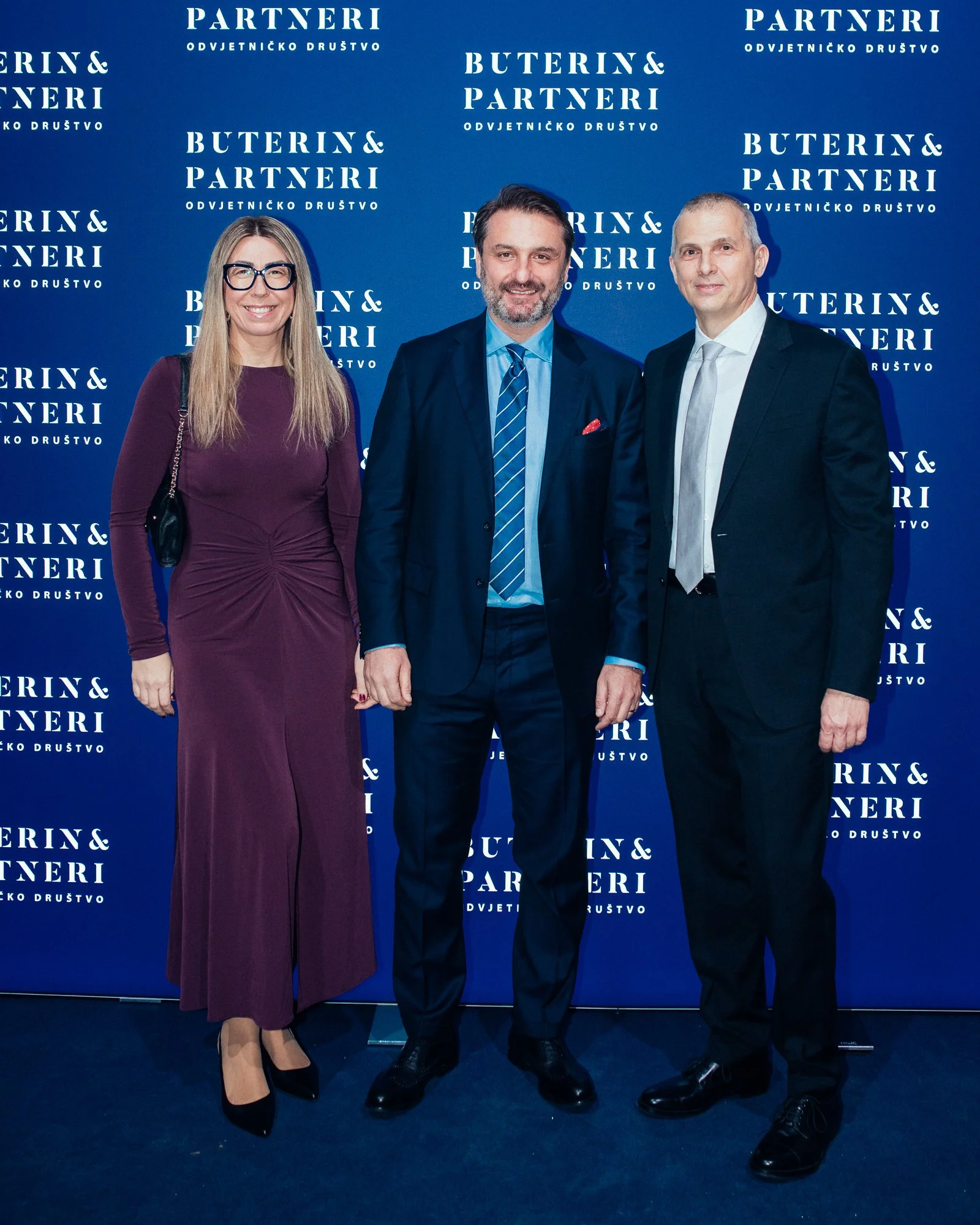 Three people dressed in formal attire standing in front of a blue backdrop with white text that reads 'PARTNERI ODVIJETNICKO DRUŠTVO' and 'BUTERIN & PARTNERI'.