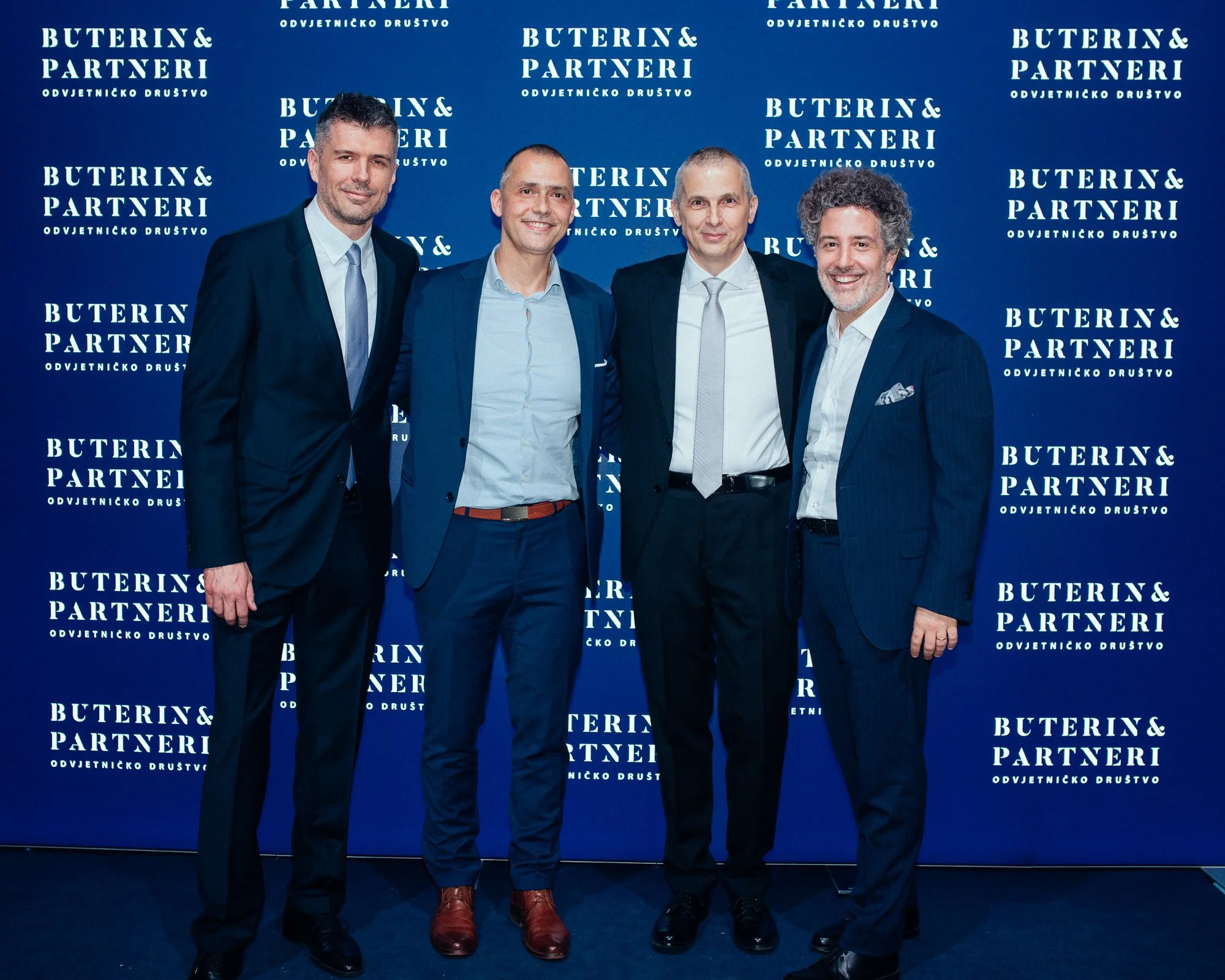 Four men in suits standing together in front of a blue backdrop with the text 'Buterin & Partneri'.