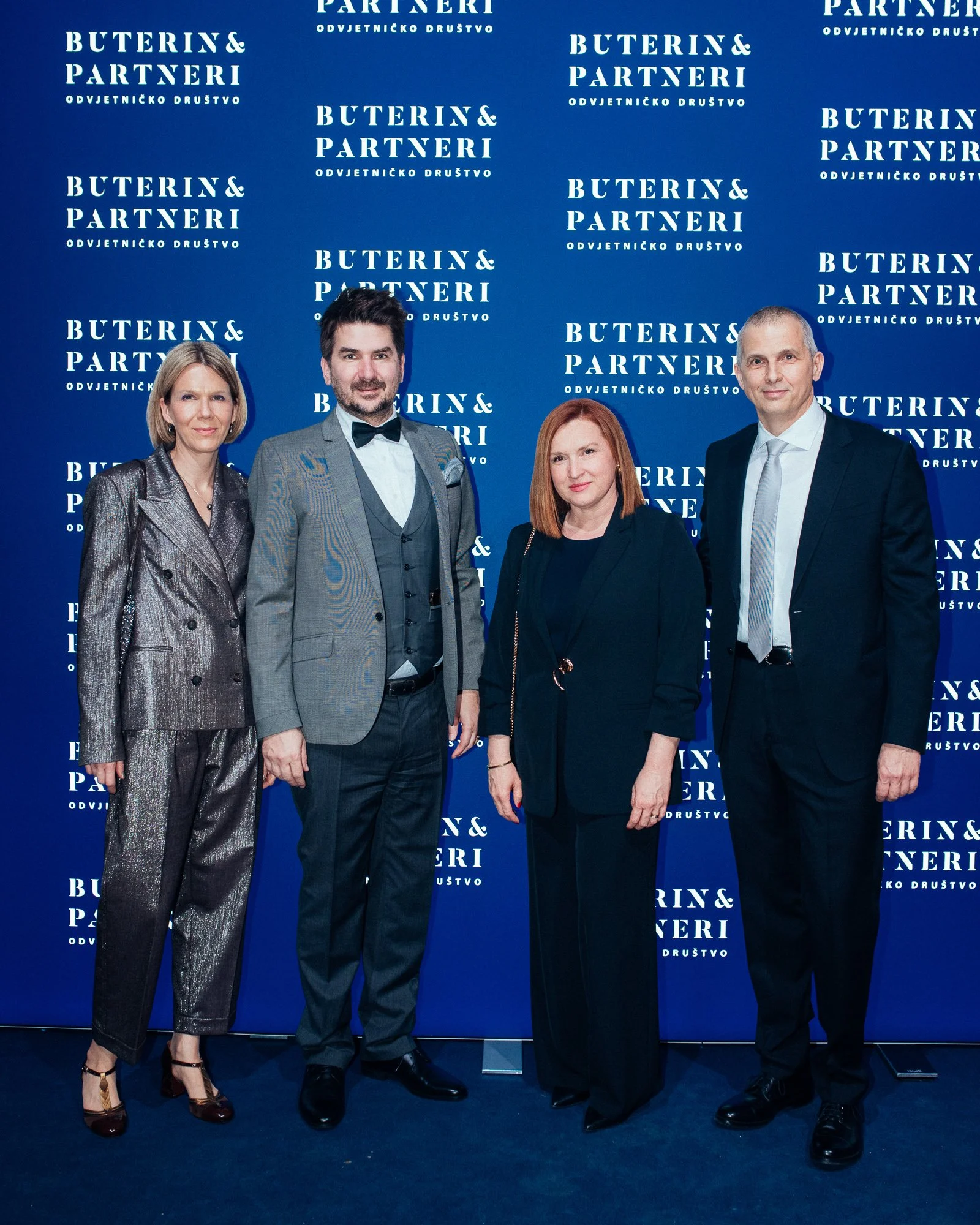 Four people dressed in formal attire standing in front of a blue backdrop with white text that reads 'Buterin & Partneri Odvjetničko Društvo'.