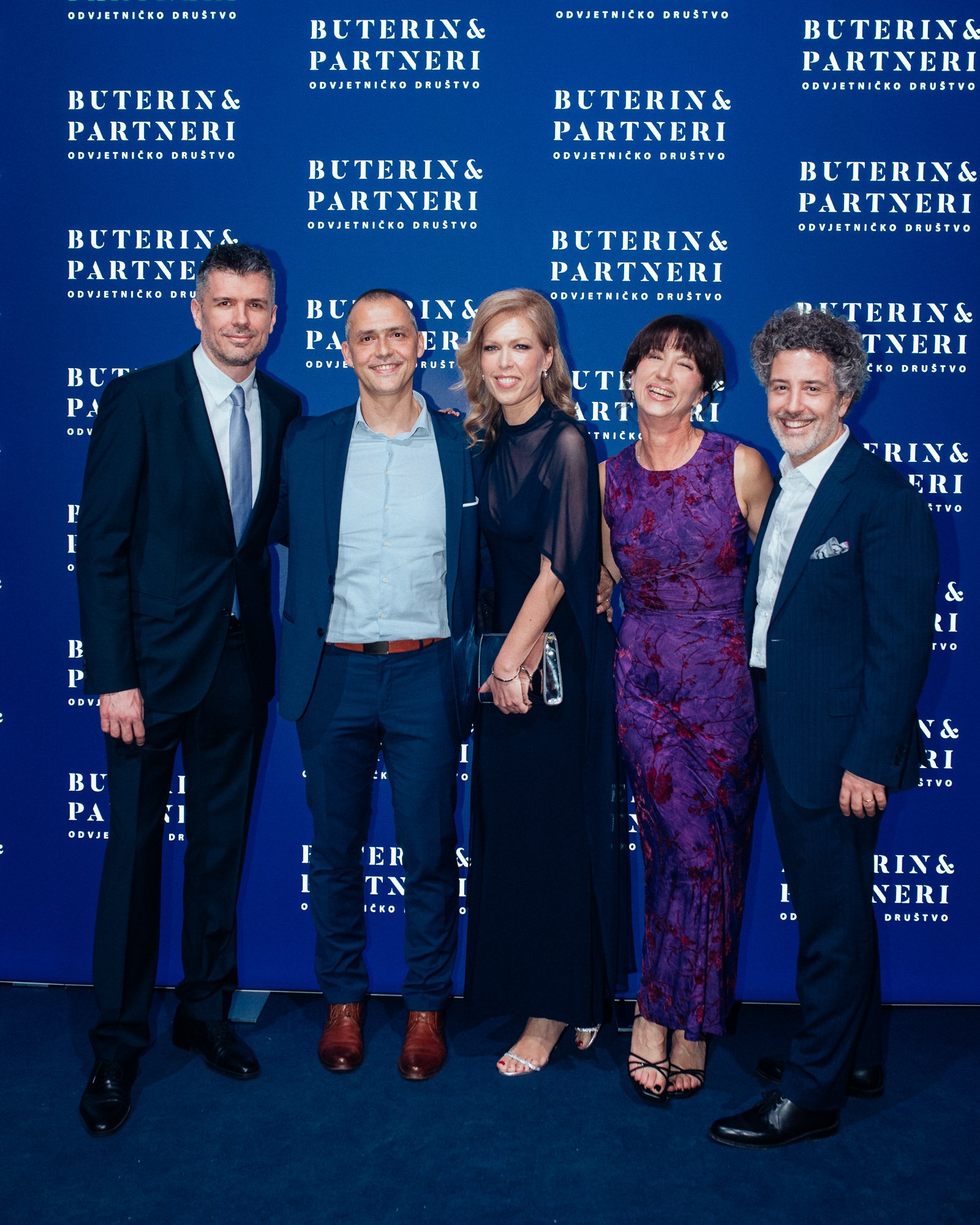 Five people in formal attire standing together in front of a blue backdrop with the words 'Buterin & Partneri' and 'Odvjetničko društvo' repeated multiple times.