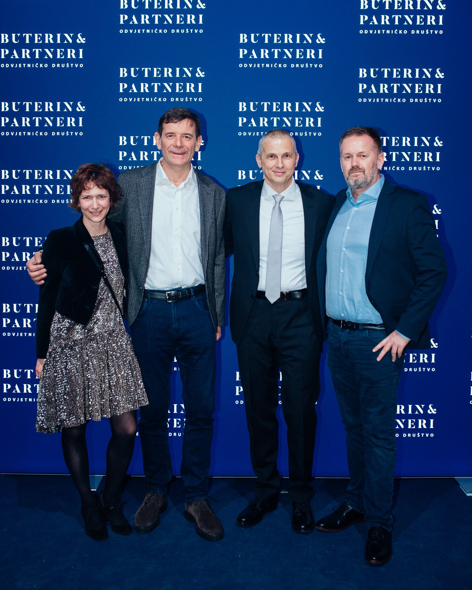 Four people standing in front of a blue backdrop with white text that reads 'Buterin & Partneri' and 'Odvjetničko Društvo.' They are dressed in business and semi-formal attire, smiling for the photo.