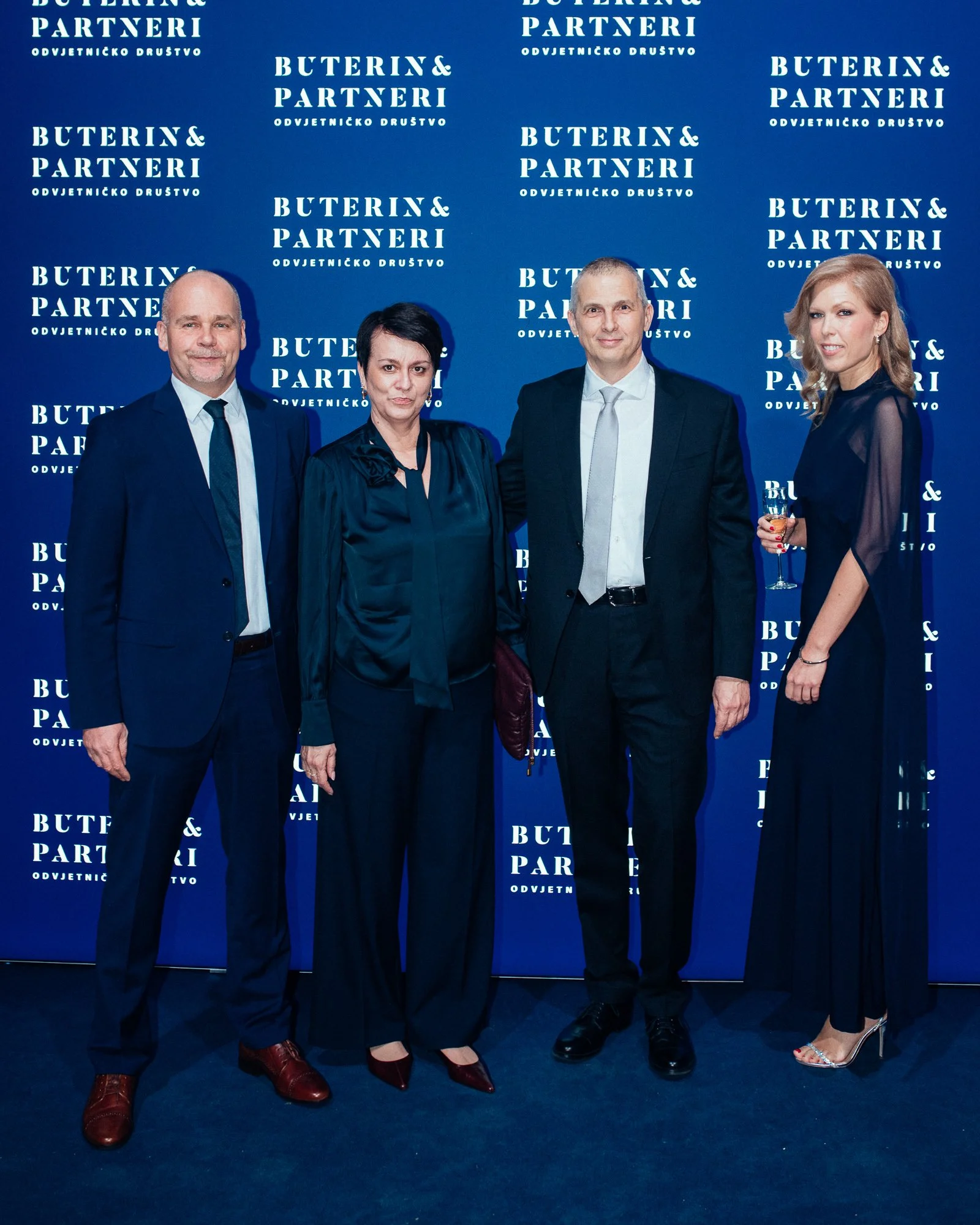 Four people dressed in formal attire standing together at an event, in front of a blue backdrop with the words 'Buterin & Partneri' and 'Odvjetničko Društvo' repeated.