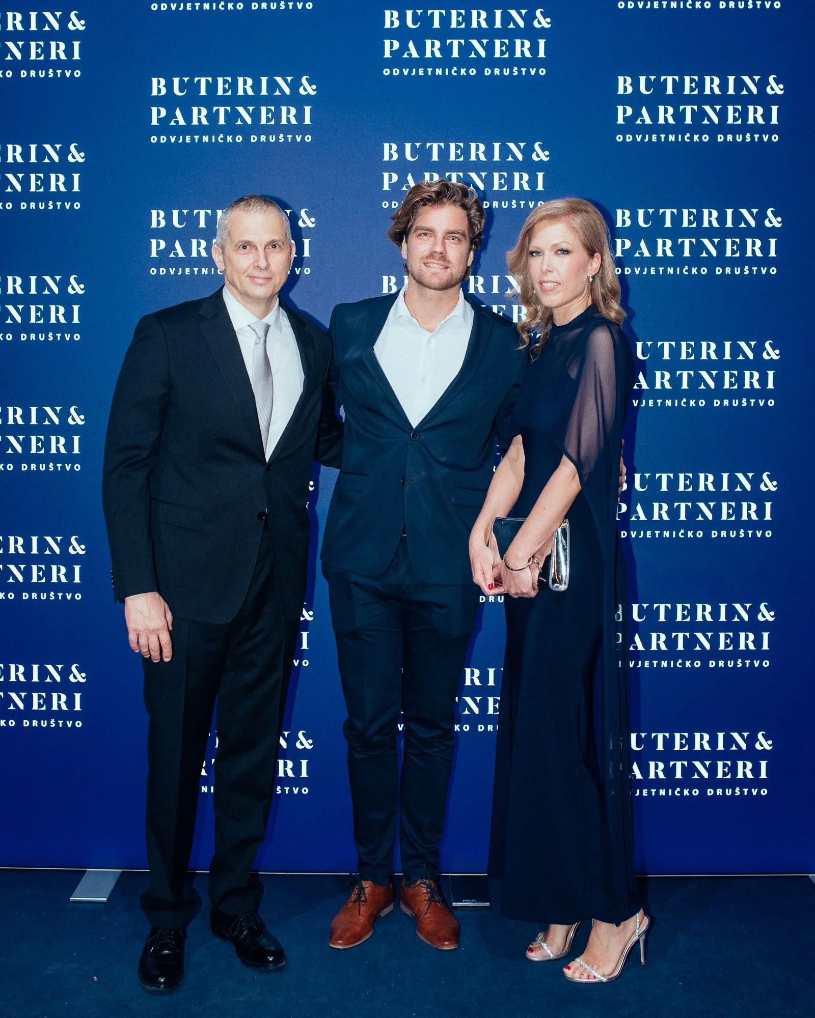 Three people in formal attire standing in front of a blue backdrop with white text that reads 'Buterin & Partneri Odvjetničko Društvo'.