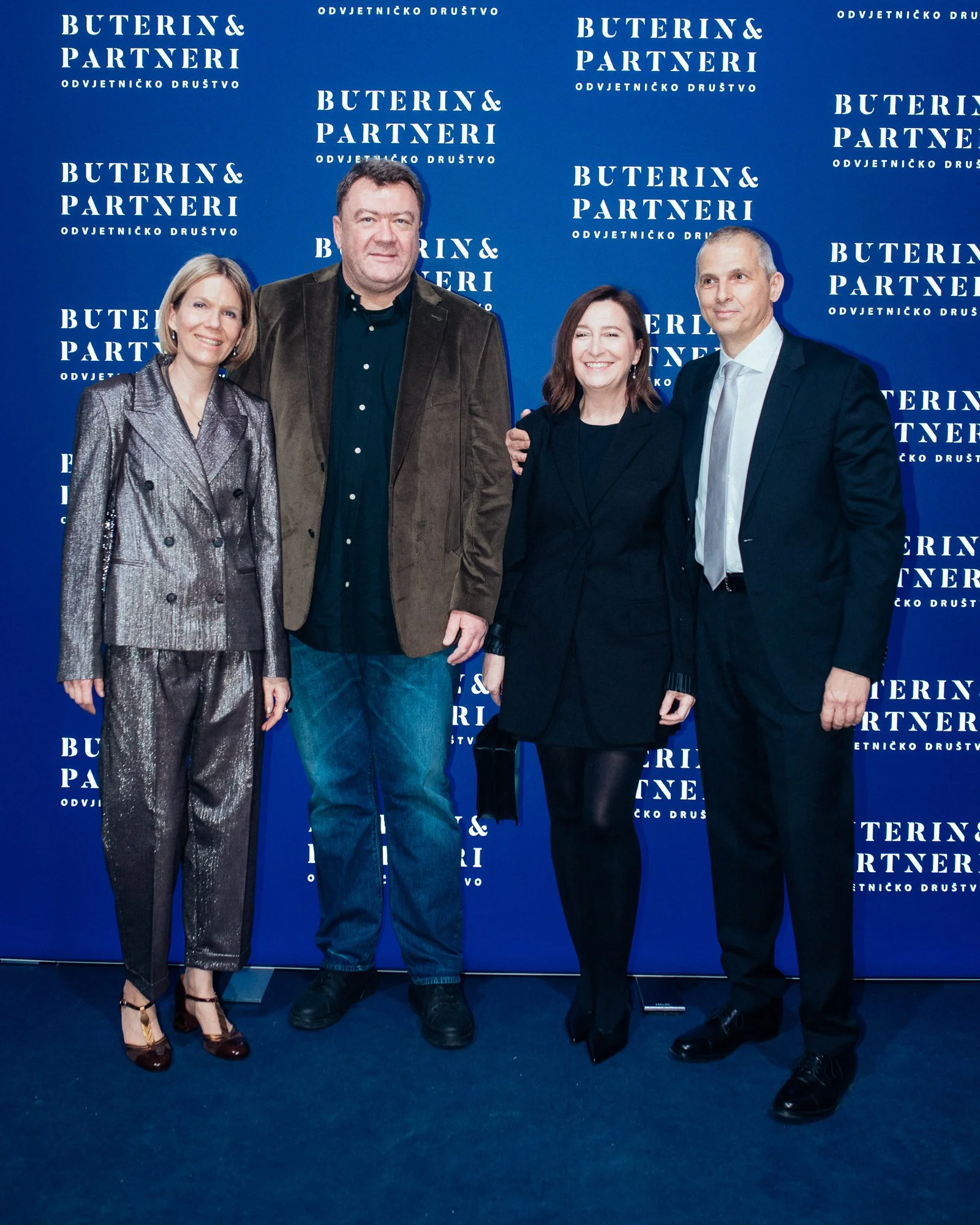 Four people standing together in front of a blue backdrop with white text reading "Buterin & Partneri" and "Odvjetničko Društvo." They are dressed in formal and semi-formal attire, smiling for the photo.