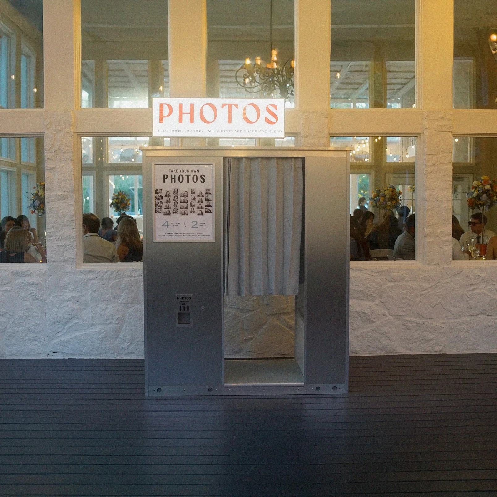 Photo booth with a curtain for taking self-portraits at a social event or wedding reception, with a sign above that says 'PHOTOS'.