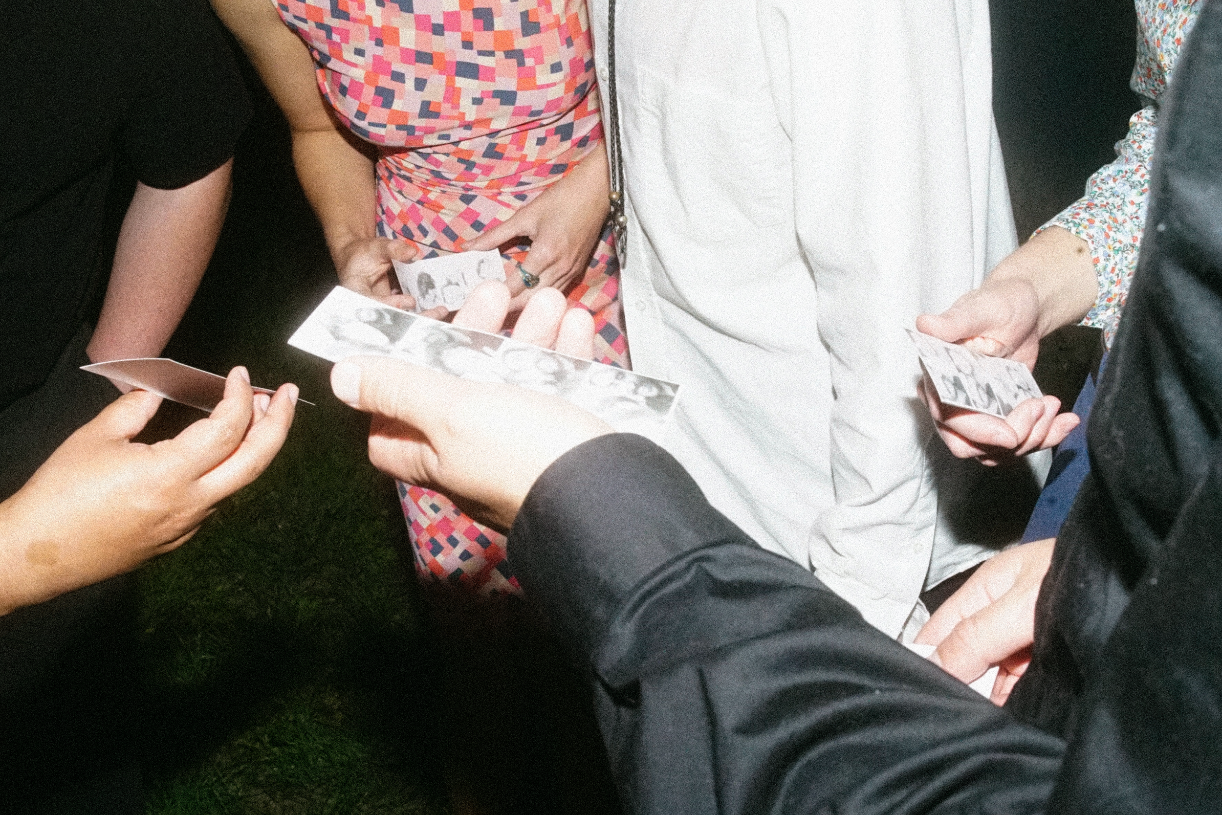 People at a wedding  gathered in a circle holding and looking at black and white photo strips.