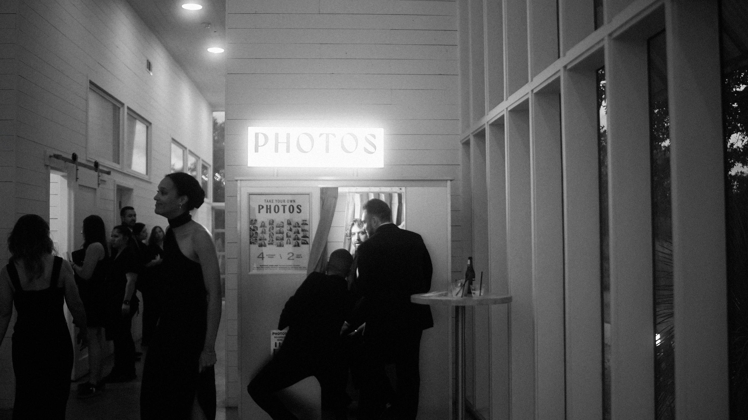 People at a photo booth with a sign that reads 'PHOTOS' at a wedding.