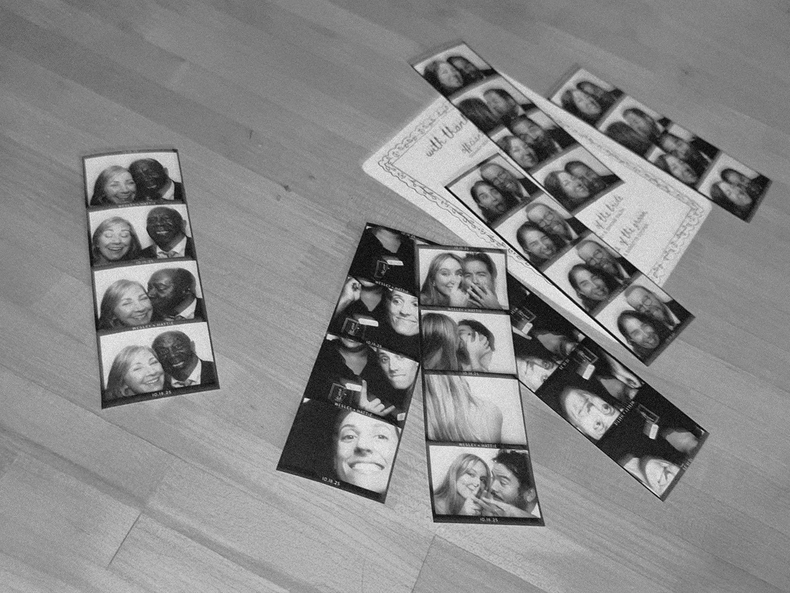 Multiple photo booth strips with various group and individual portraits of people, some smiling and making funny faces, laid out on a wooden table alongside a wedding program.