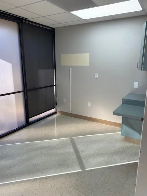 Empty medical office with sliding glass door, beige wall with a blank yellowish poster, and blue cabinets.