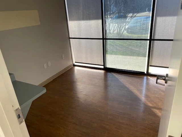 Empty room with wooden flooring, large window with a net curtain, and a built-in shelf on the wall.