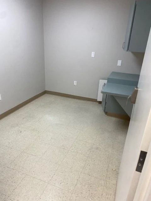 Empty room with gray walls, beige baseboards, off-white tiled floor, and a gray wall-mounted desk or cabinet.
