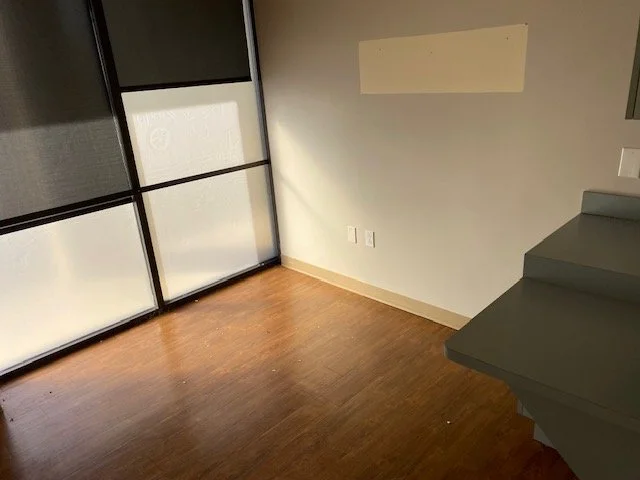 Empty room with wooden flooring, frosted glass sliding door, and a staircase on the right side.