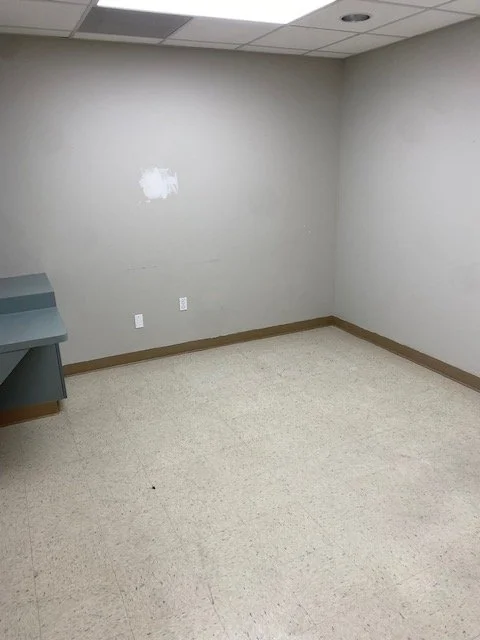 Empty room with beige carpet, gray walls, a small built-in desk on the left, and a patch of paint on the wall.
