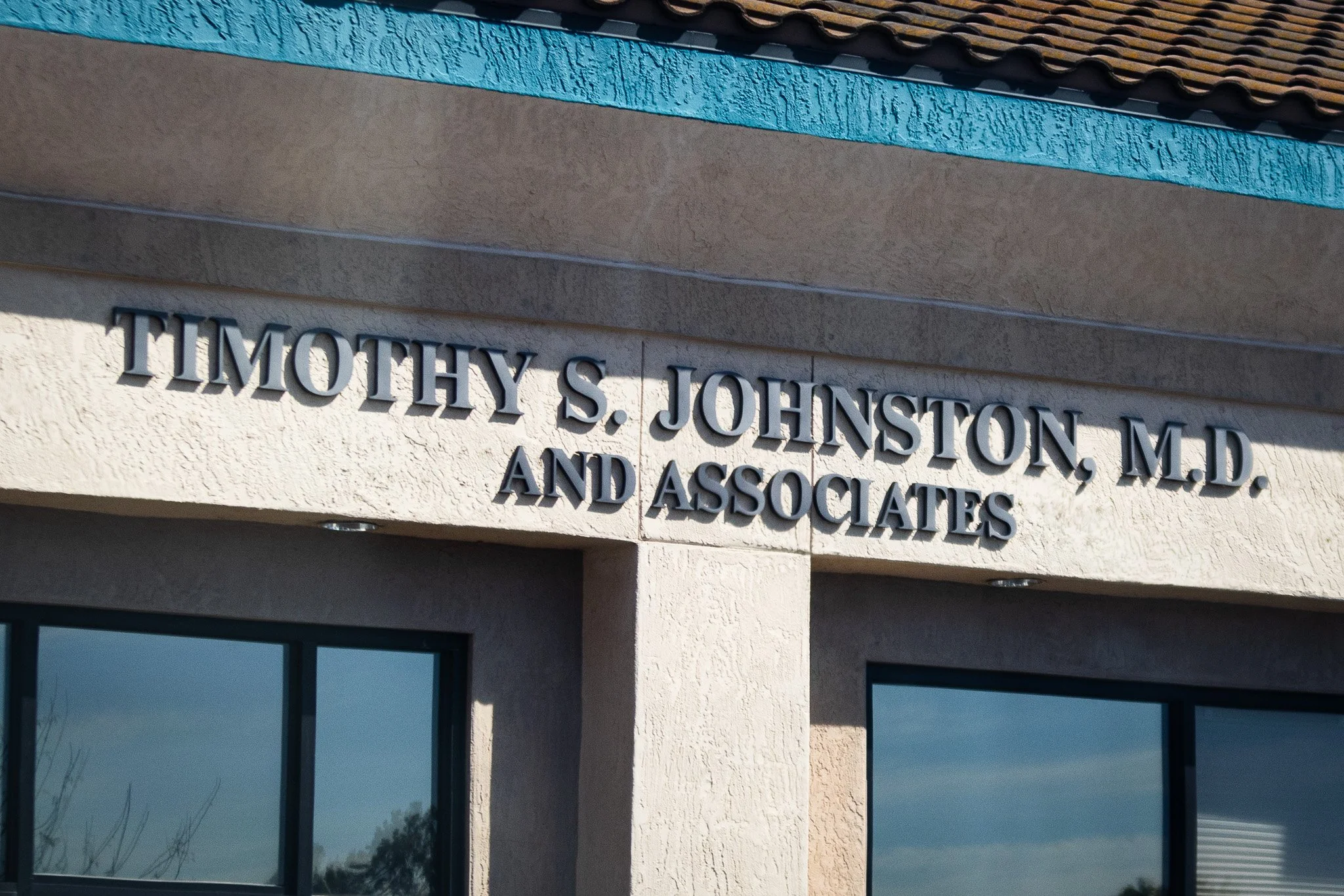 Sign on a building reading 'Timothy S. Johnston, M.D. and Associates' in silver letters against a light-colored textured wall.