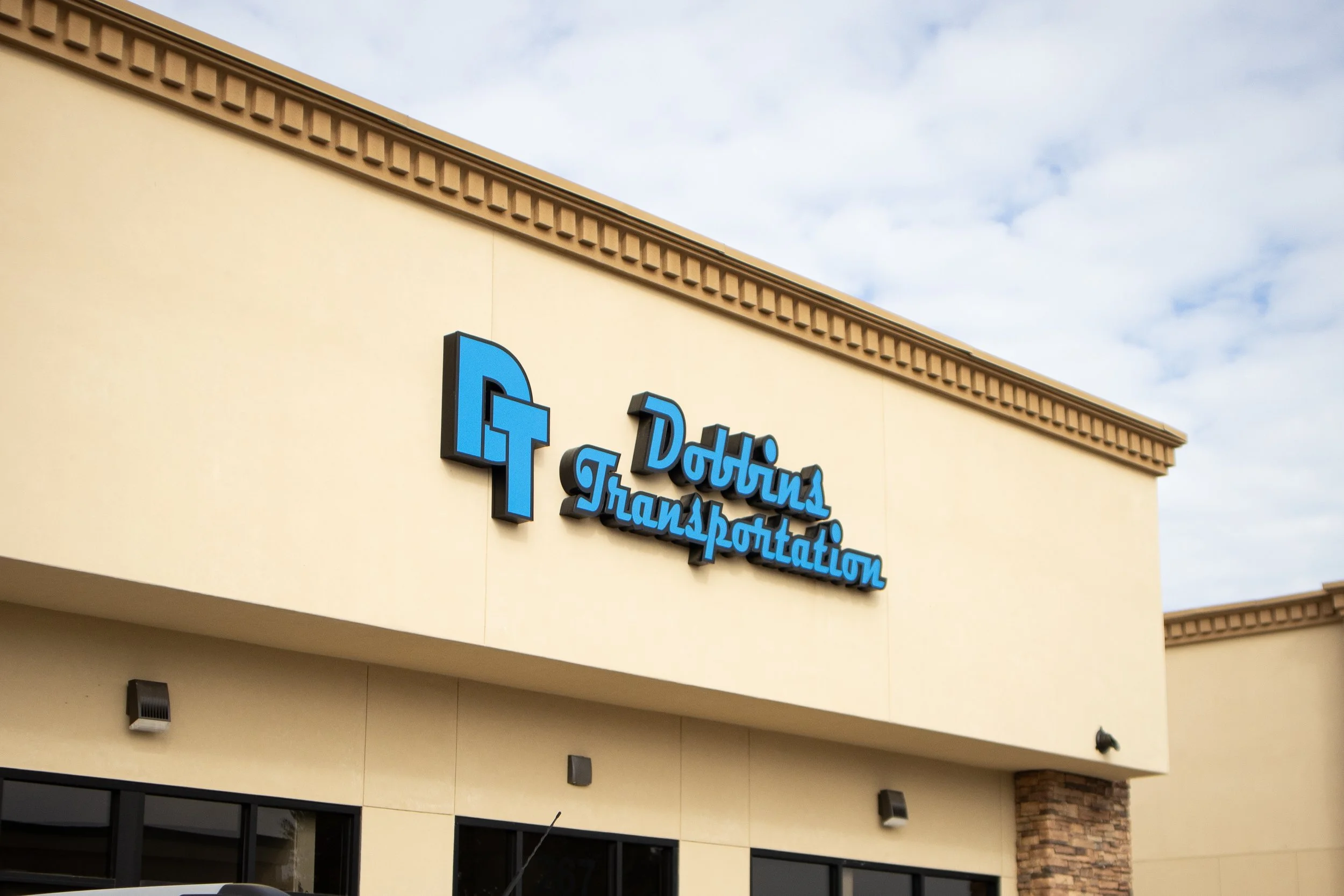 The exterior of a building with a sign that reads 'Dothin Transportation' along with a blue logo, under a cloudy sky.