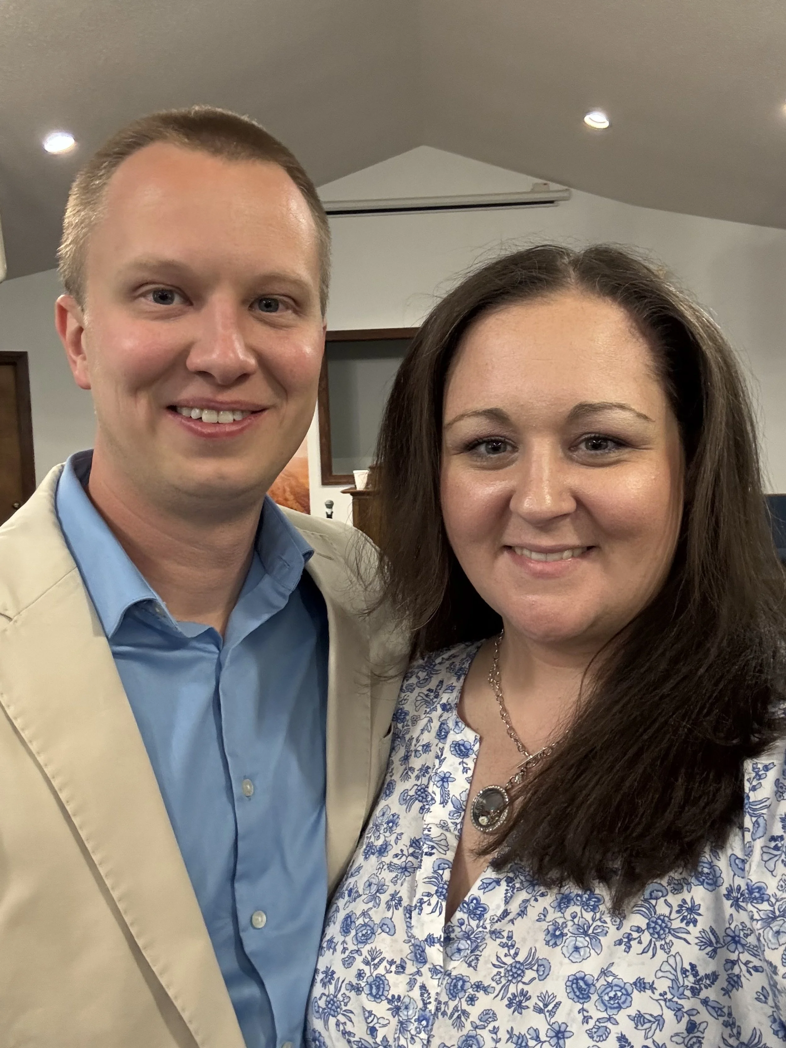 A man and woman smiling and posing for a photo indoors, standing close together.