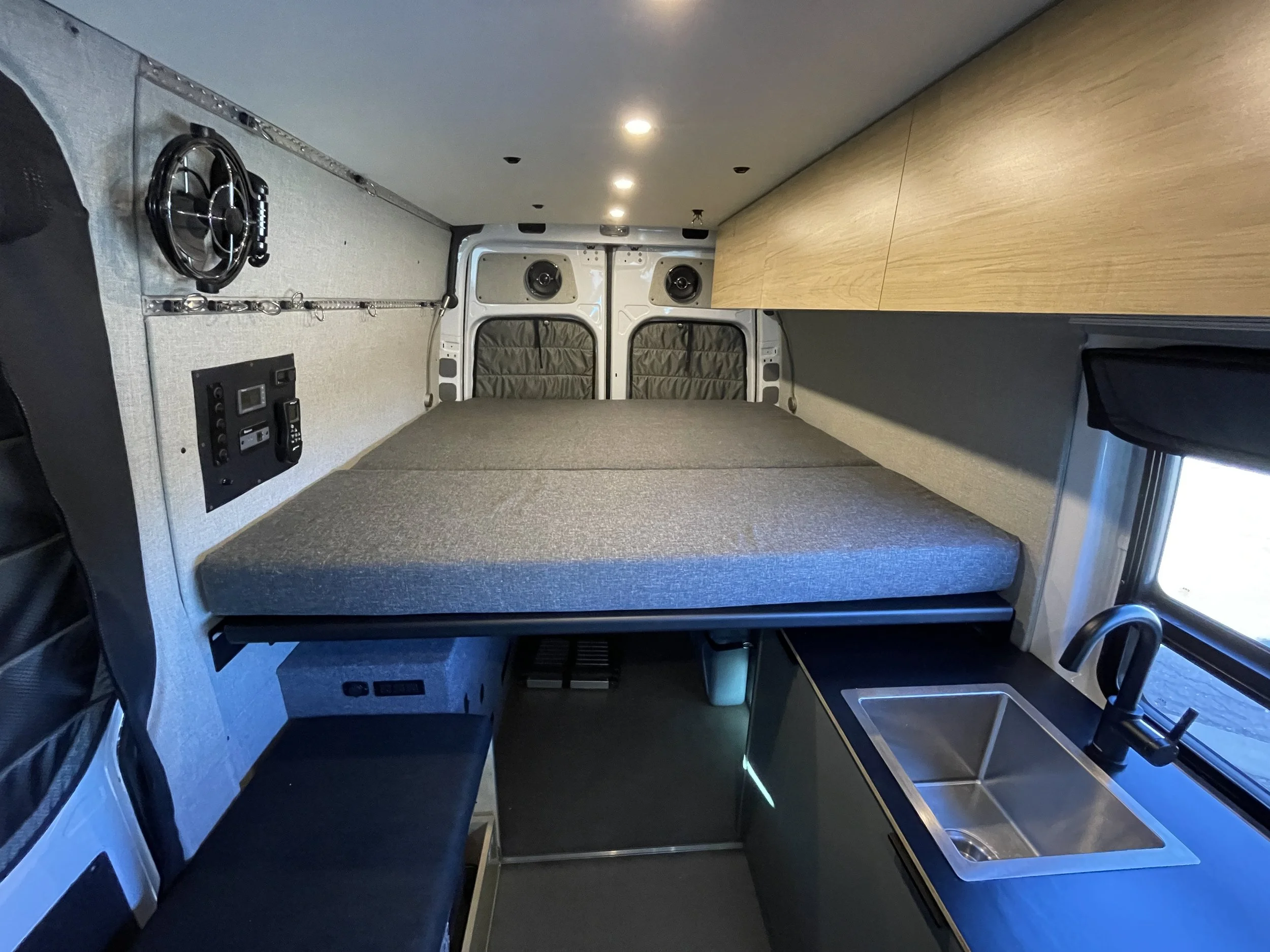 Interior of a camper van with a bed, kitchen sink, and storage space.