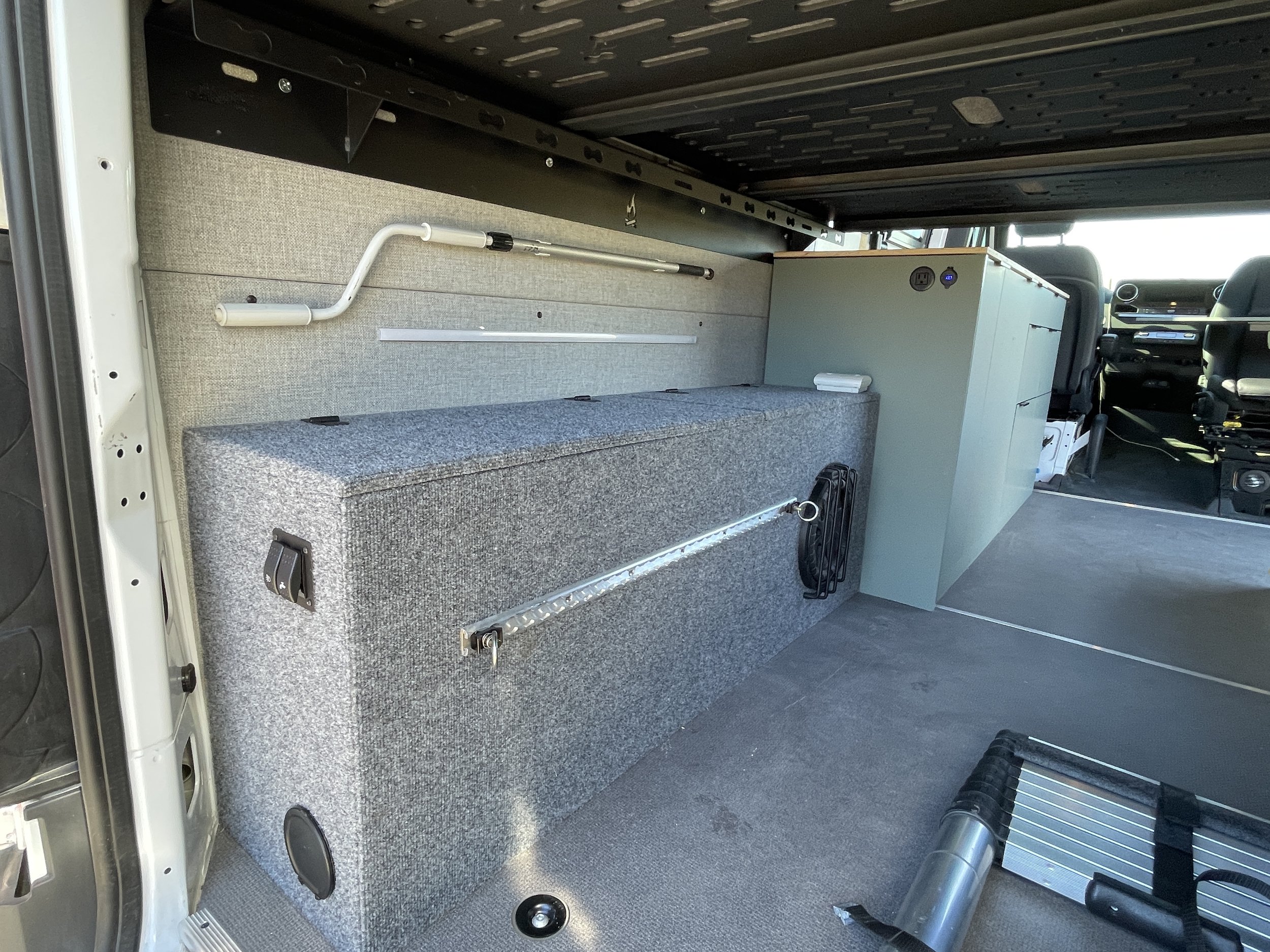 Interior of a van with a custom-built storage compartment and gray carpeting.