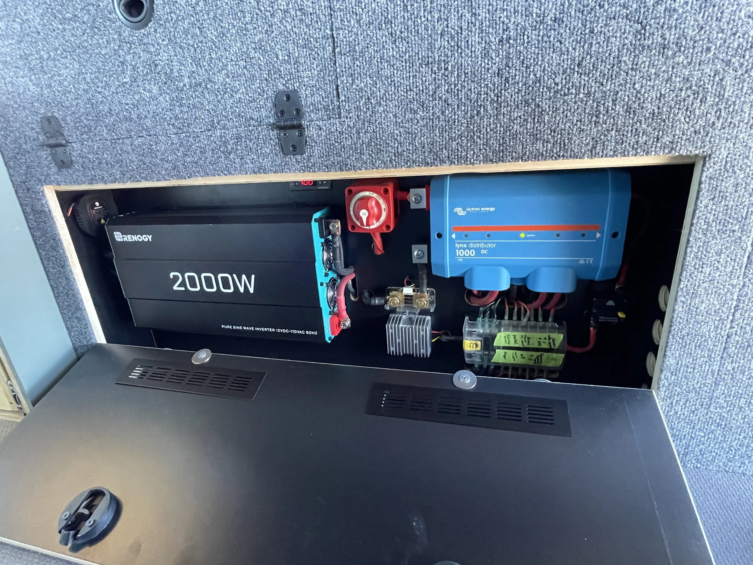 Power inverter and electrical setup in a cabinet, featuring a 2000W Renogy pure sine wave inverter and Victron Energy Lynx distributor.