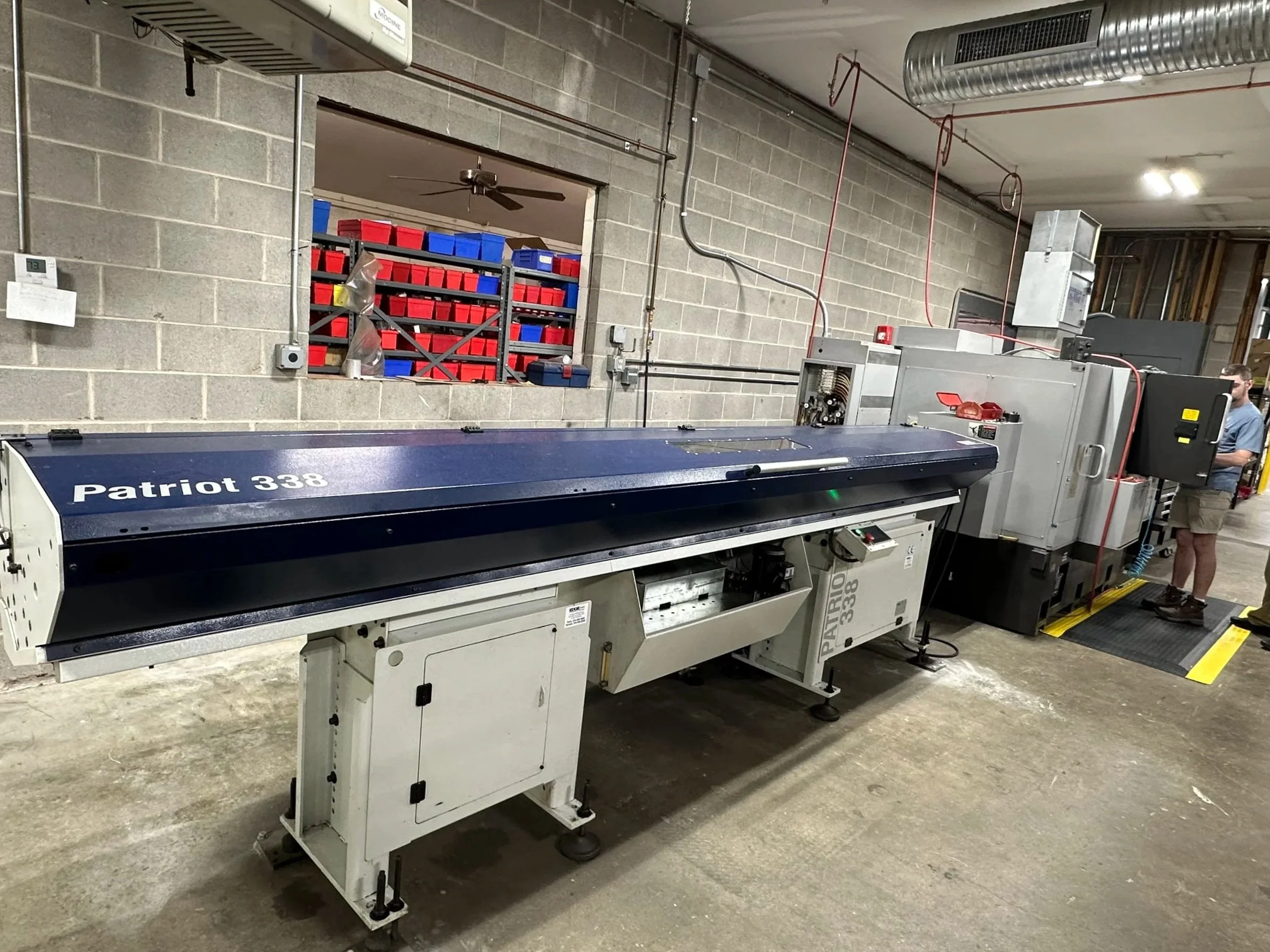 A large industrial printing machine labeled 'Patriot 338' in a warehouse setting, with various tools and storage bins in the background.
