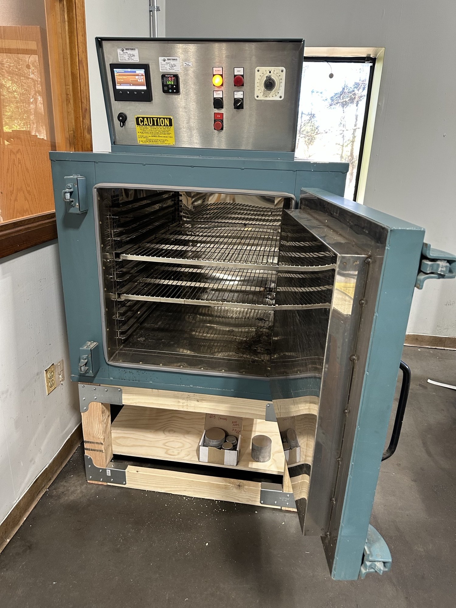 Industrial oven with open door, metal interior, control panel on top, and wooden support stand.