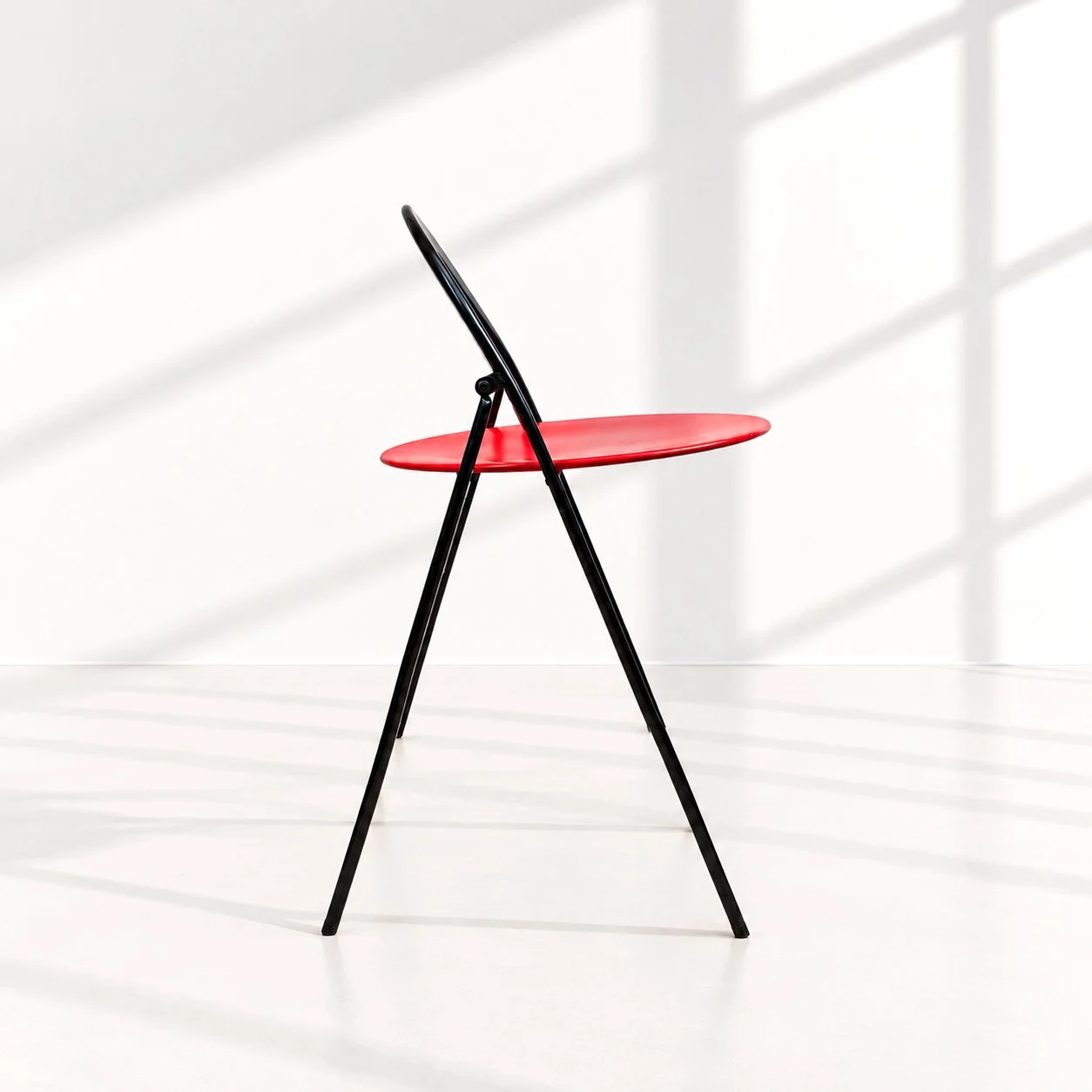 Silla Clio
A&ntilde;o: D&eacute;cada de los 70
Pa&iacute;s: Italia
Dise&ntilde;o: Giorgio Cattelan para Cidue. Una silla plegable convertida casi en un ejercicio de geometr&iacute;a: un gran arco negro envuelve el asiento circular rojo mientras estru