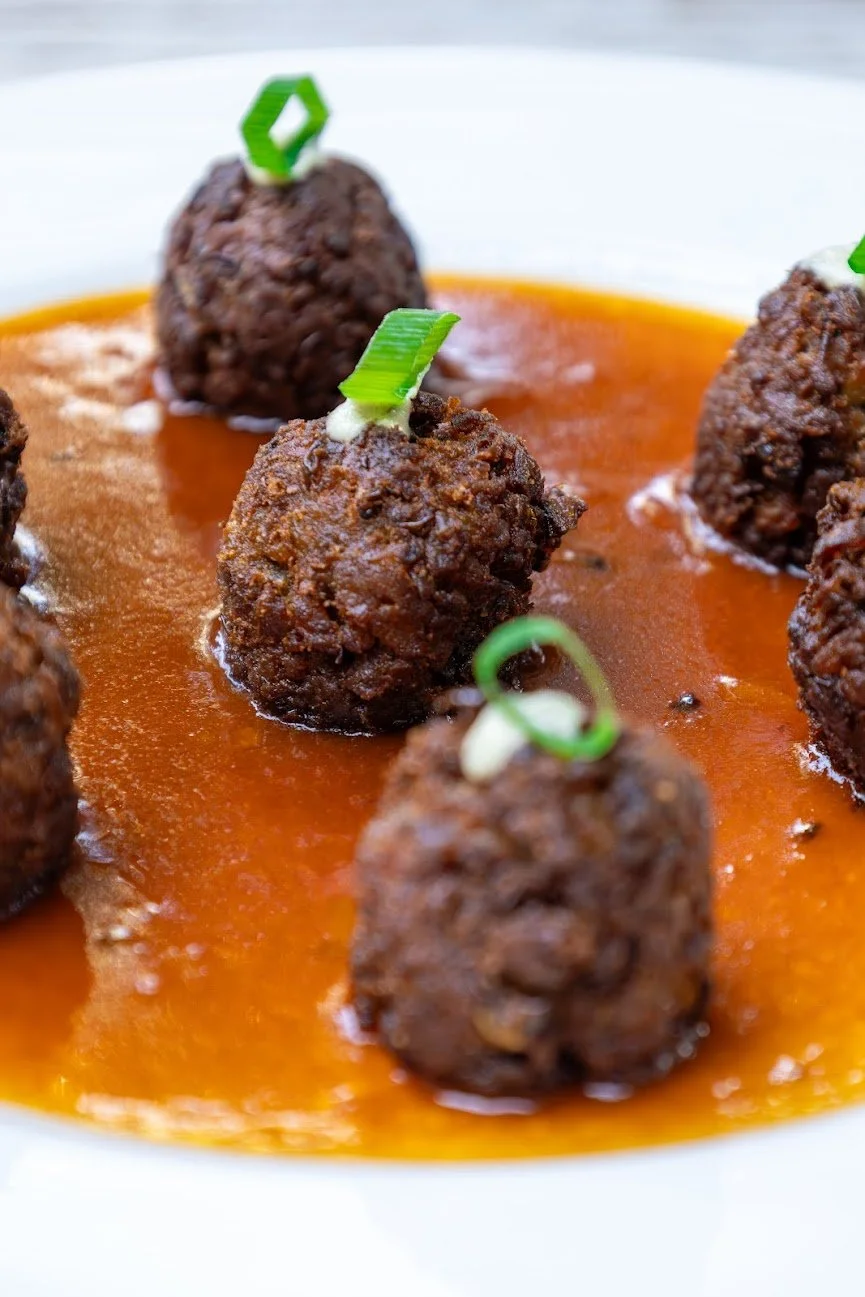 Close-up of several meatballs garnished with sliced green onions, served in a tomato sauce.