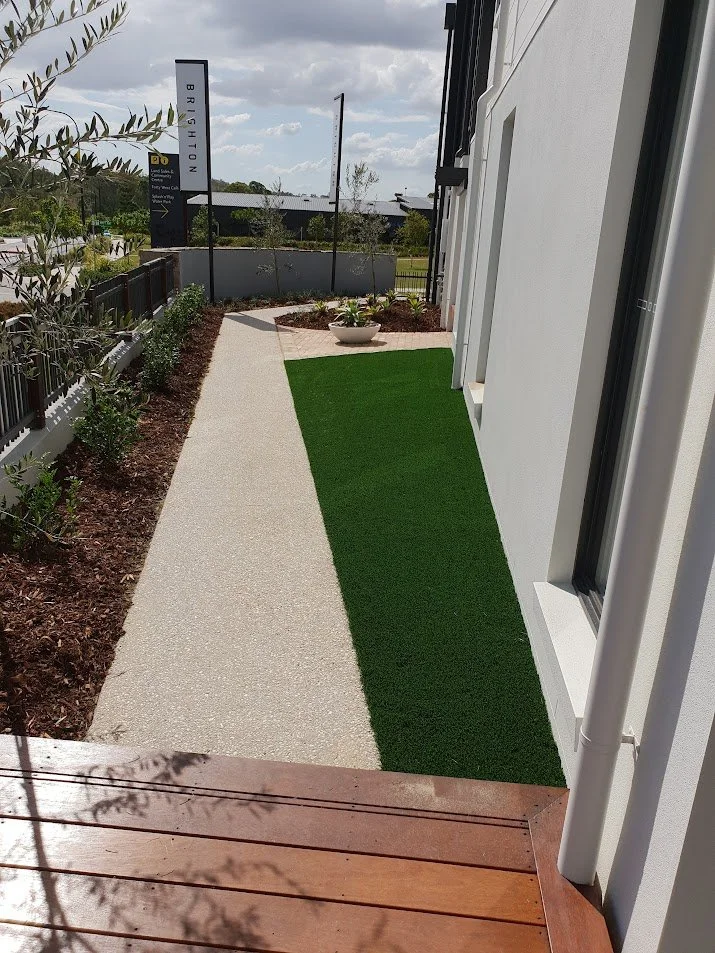 Pathway beside a building with artificial grass and landscaping