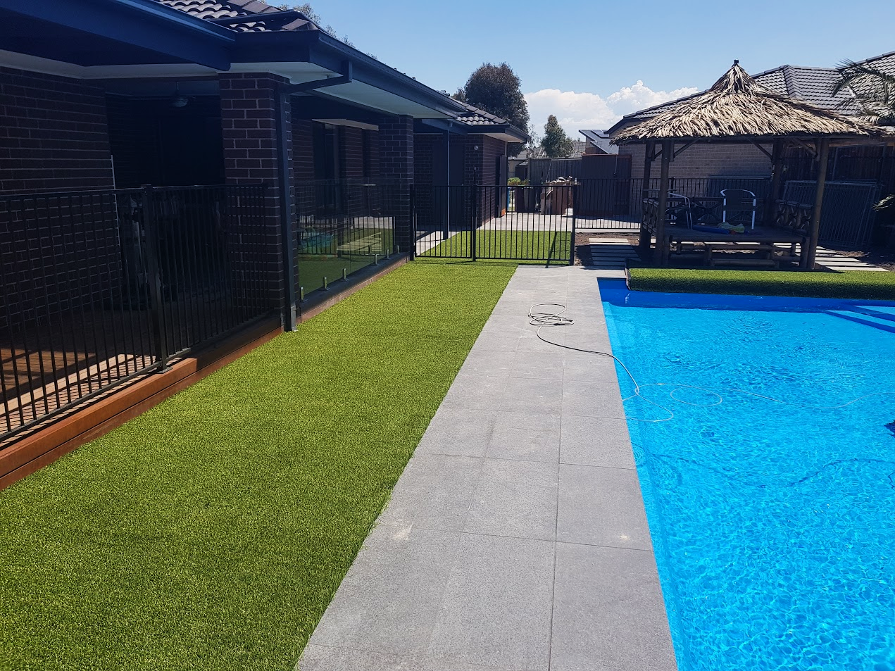 Outdoor pool area with grass, tiled walkway, and thatched gazebo.