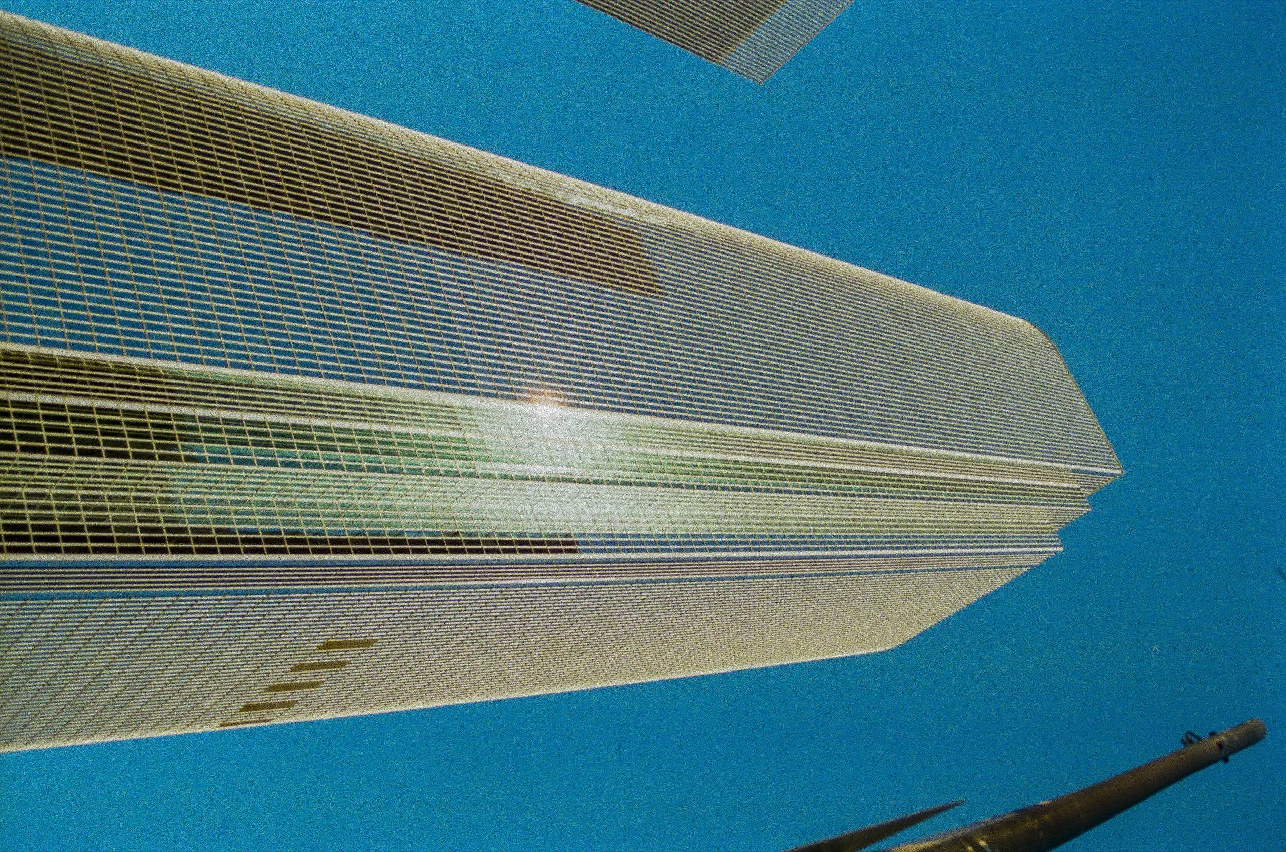 Looking up at the exterior of tall modern skyscrapers with reflective glass windows against a clear blue sky.