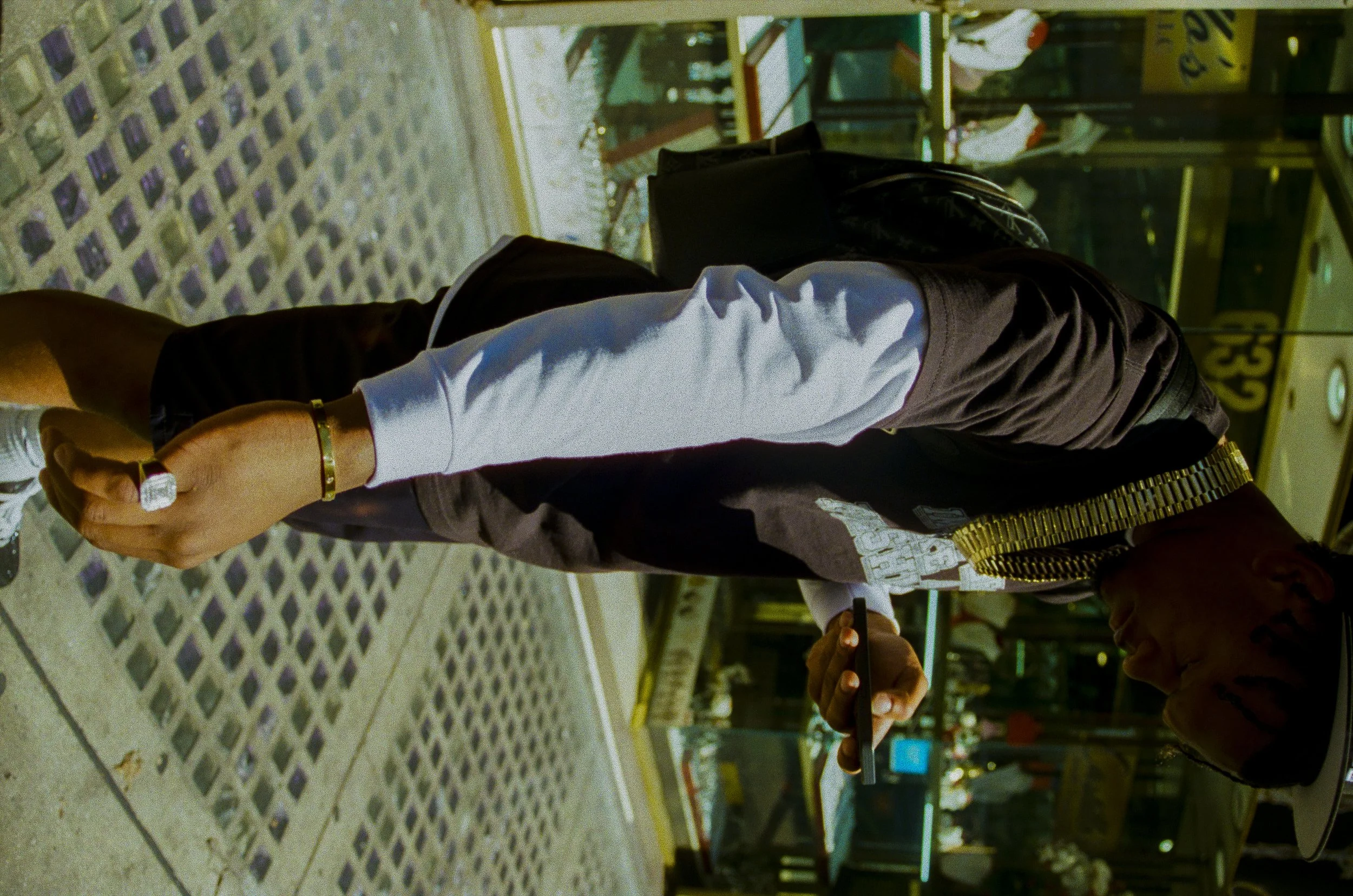 Person wearing white shirt and black jacket holding a smartphone in front of another person in a store or industrial setting.