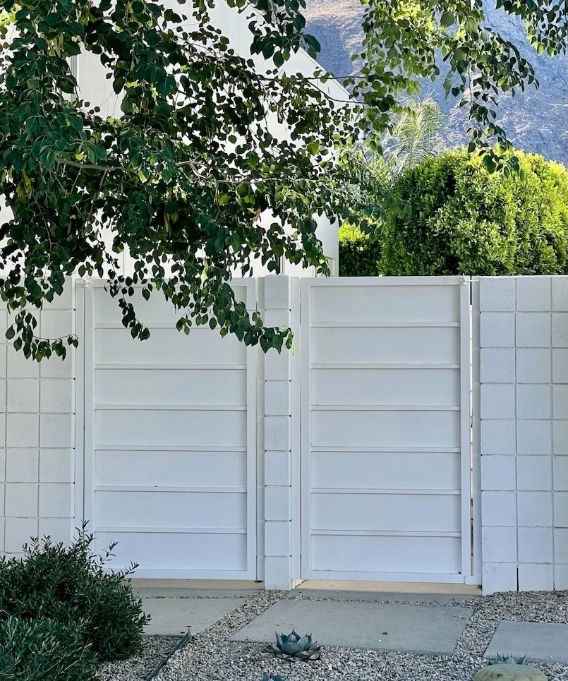 two white side yard entry gates each with a latch at the top and opaque panels with horizontal bars attached to a white block wall