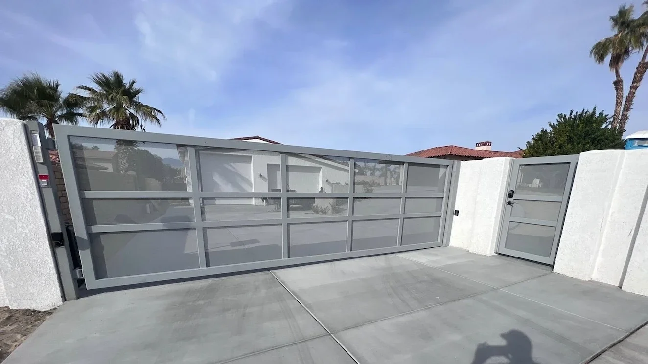 matte grey swing driveway gate with perforated mesh backing and a matching adjacent pedestrian gate at the front of a home’s concrete driveway