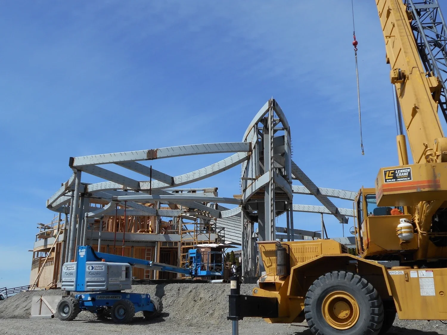 an impressive and complex structural steel base for a multi-story and uniquely designed home with blue sky behind and equipment trucks in front